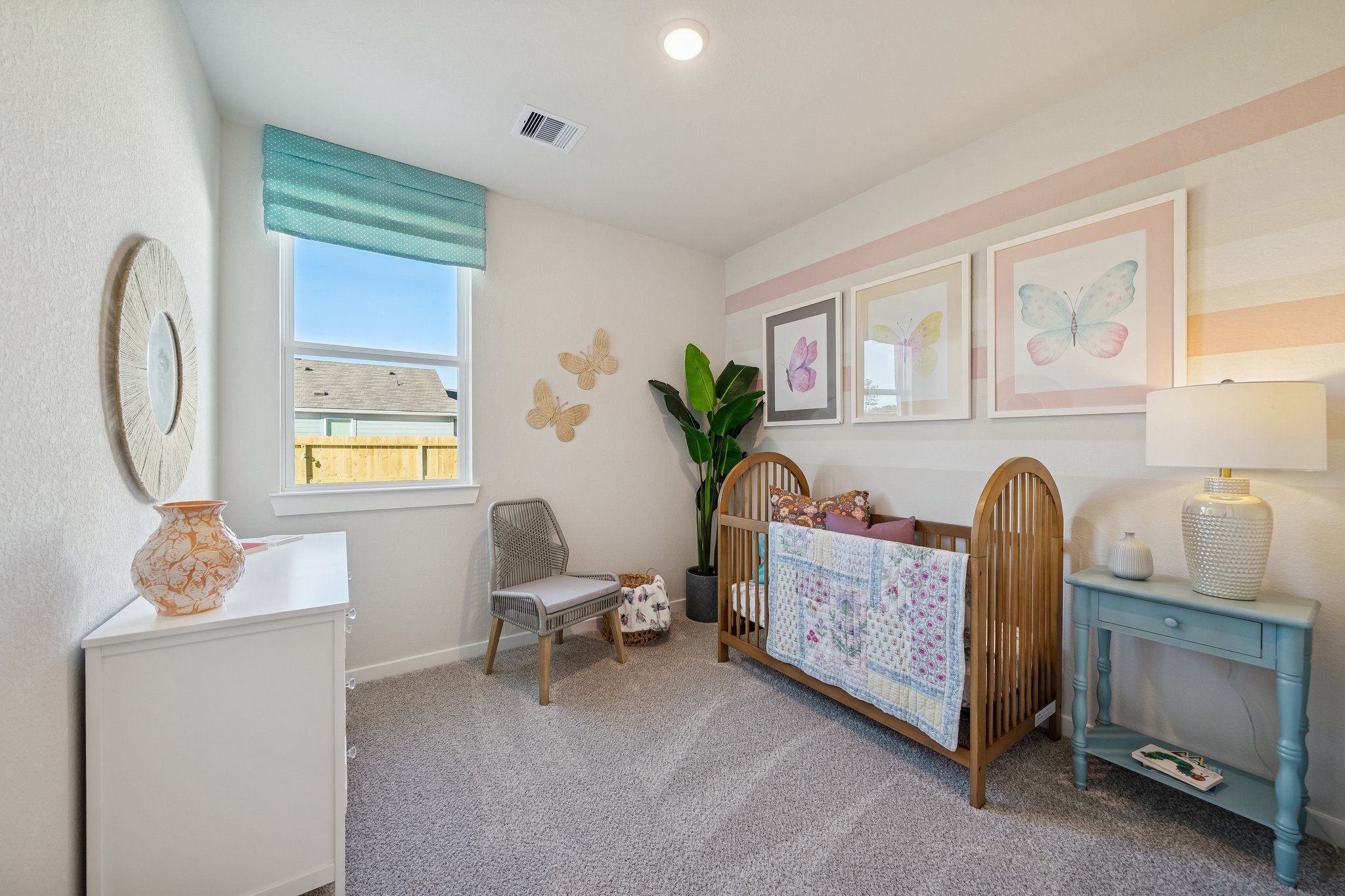 Cozy nursery at Spring Branch Crossing in Conroe TX with wooden crib, pink quilt, teal curtains, and butterfly decor