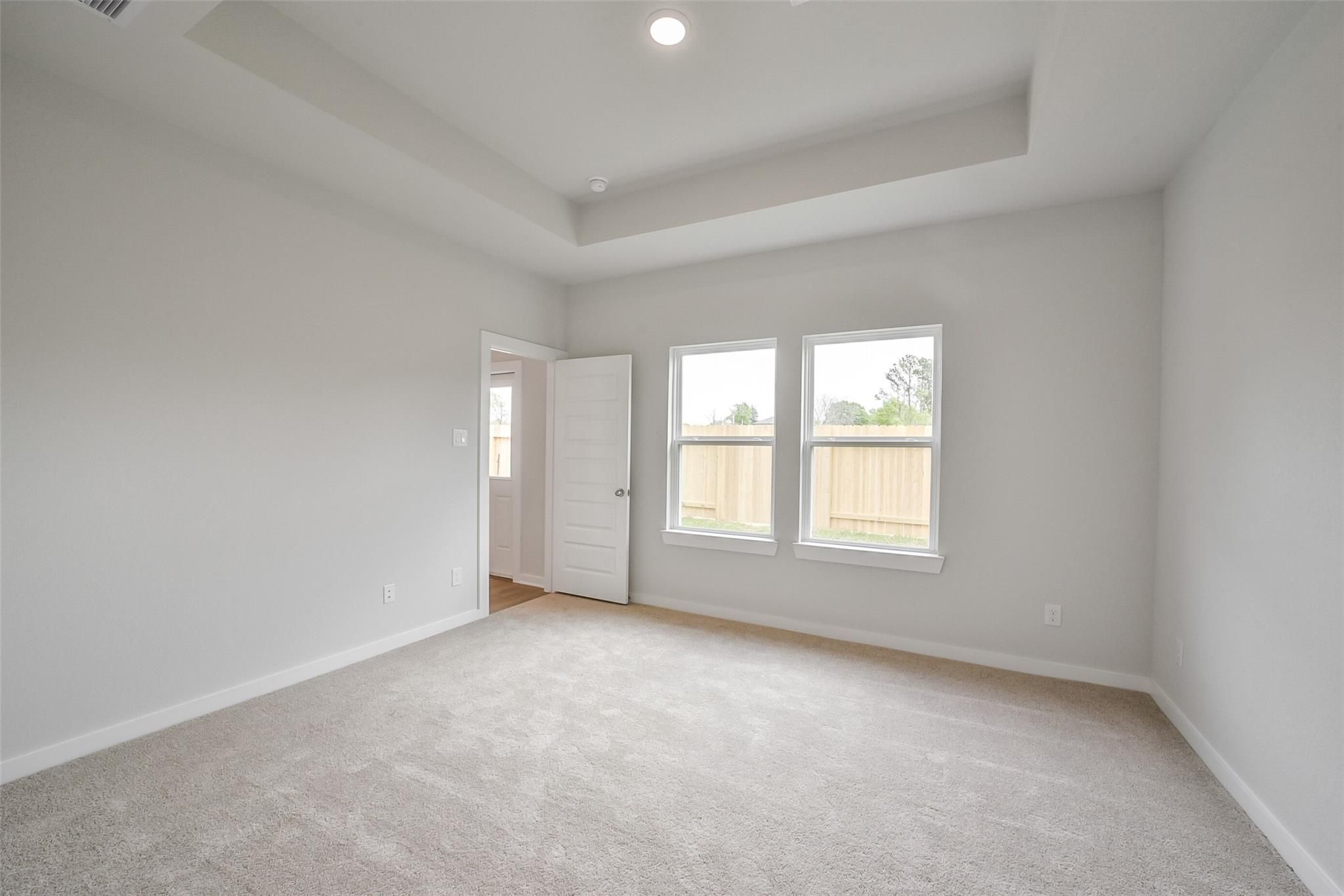 Bright master bedroom with tray ceiling, large windows to backyard fence in Davidson Homes The Frio F, Conroe, Texas