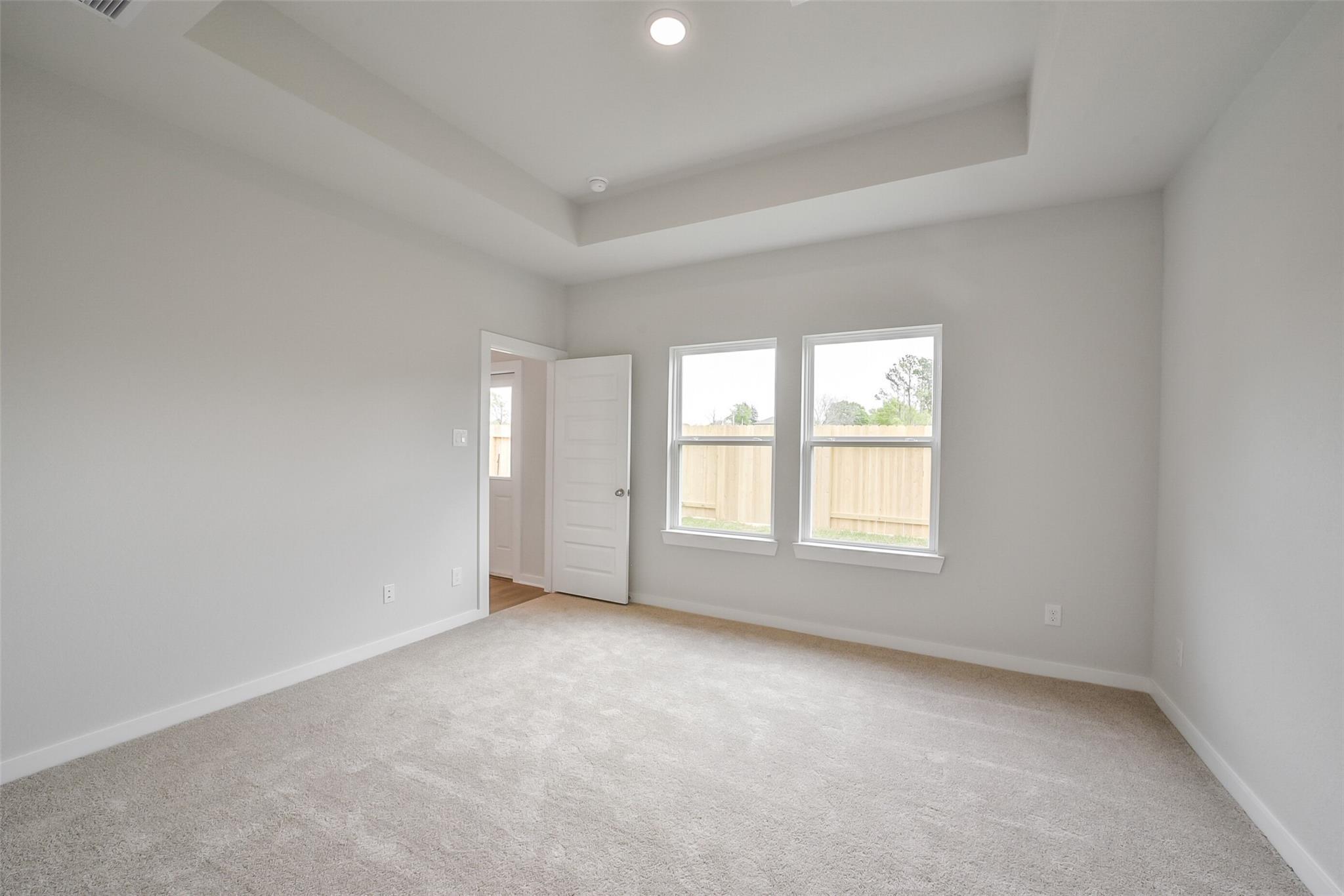 Bright master bedroom with tray ceiling, large windows to backyard fence in Davidson Homes The Frio F, Conroe, Texas