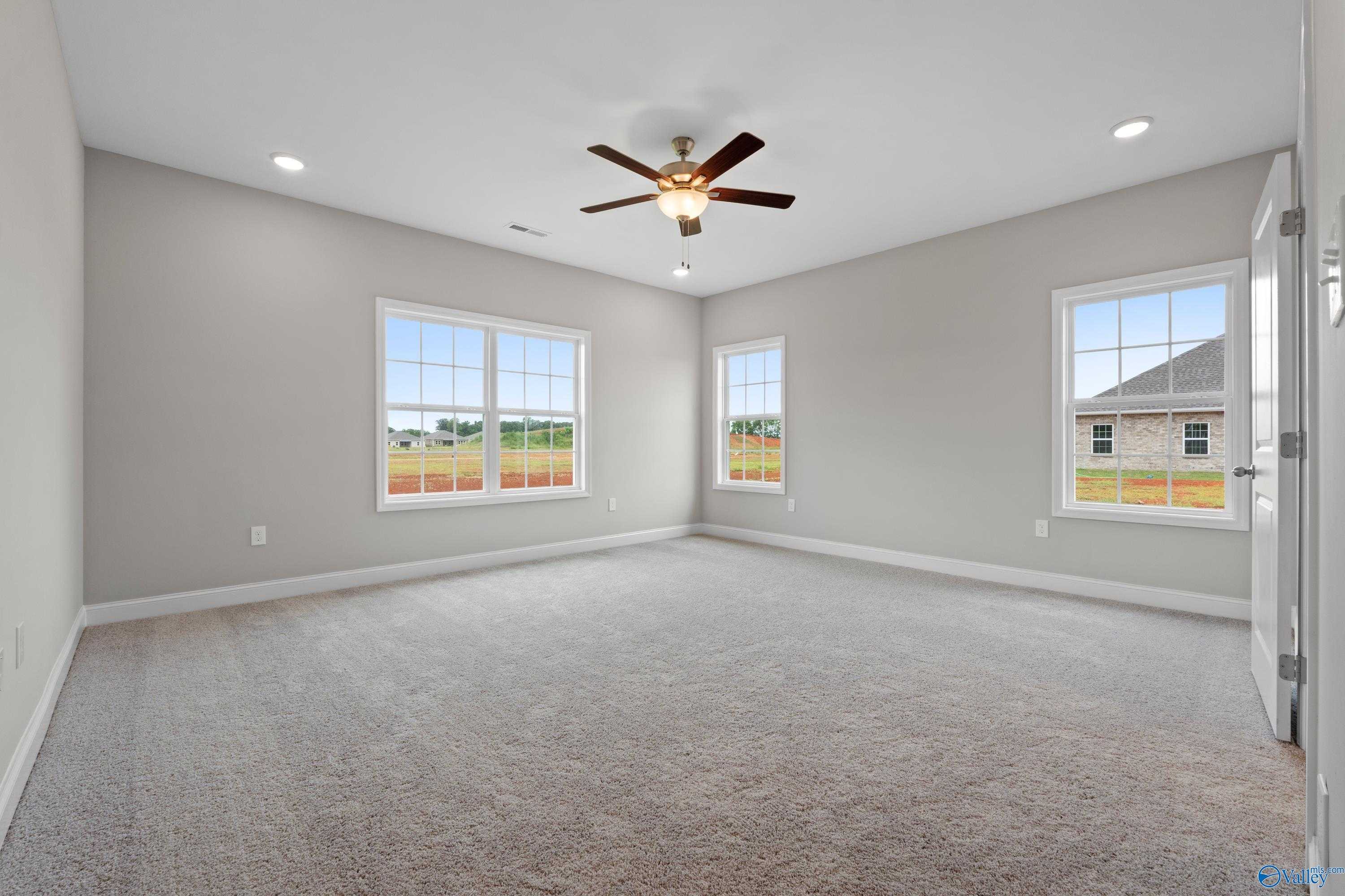 Spacious empty bedroom with light gray walls, beige carpet, large windows overlooking fields, ceiling fan in The Finleigh by Davidson Homes, Meridianville AL