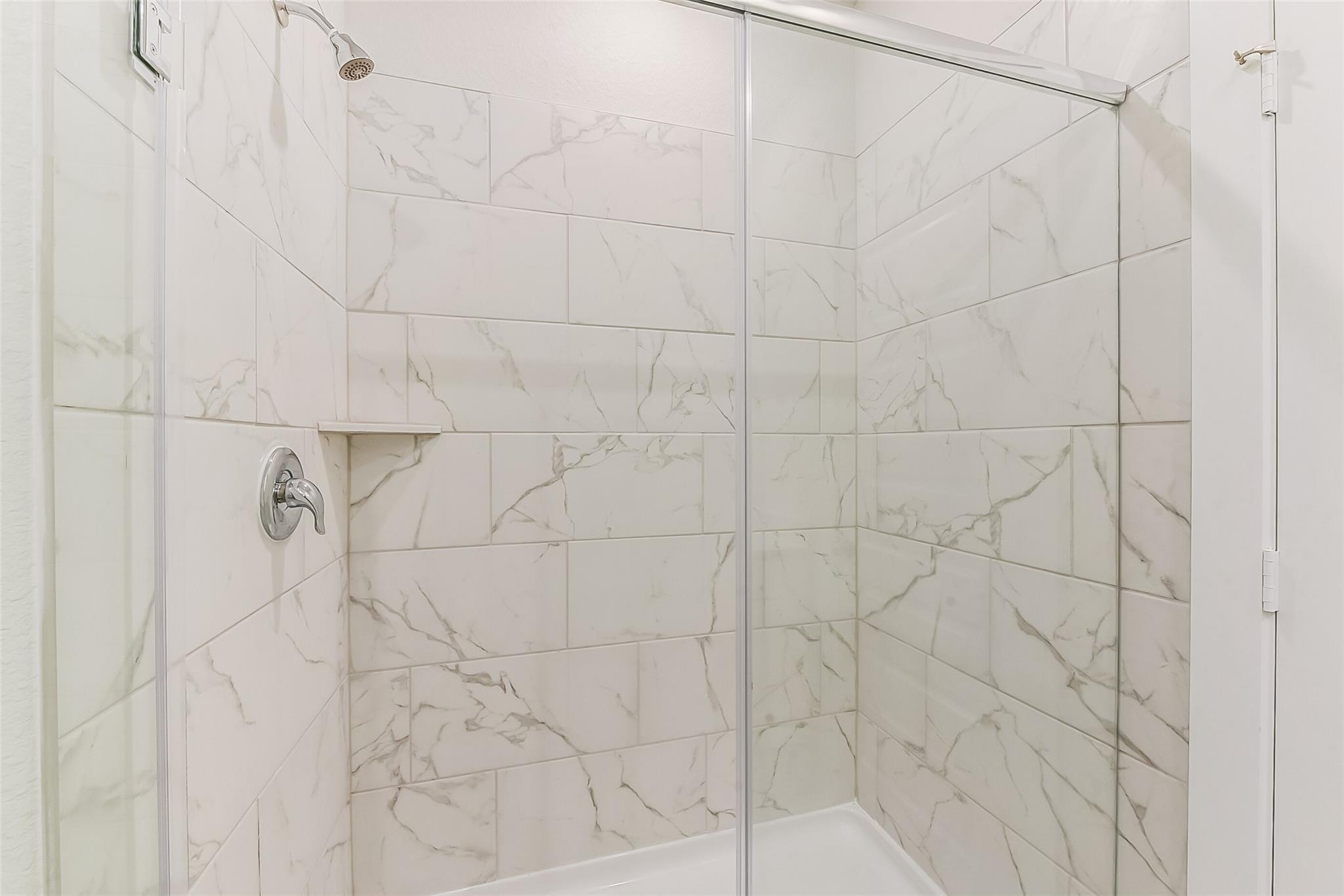 Elegant frameless glass shower with white marble-veined subway tiles in master bath, The Frio G by Davidson Homes, Magnolia TX