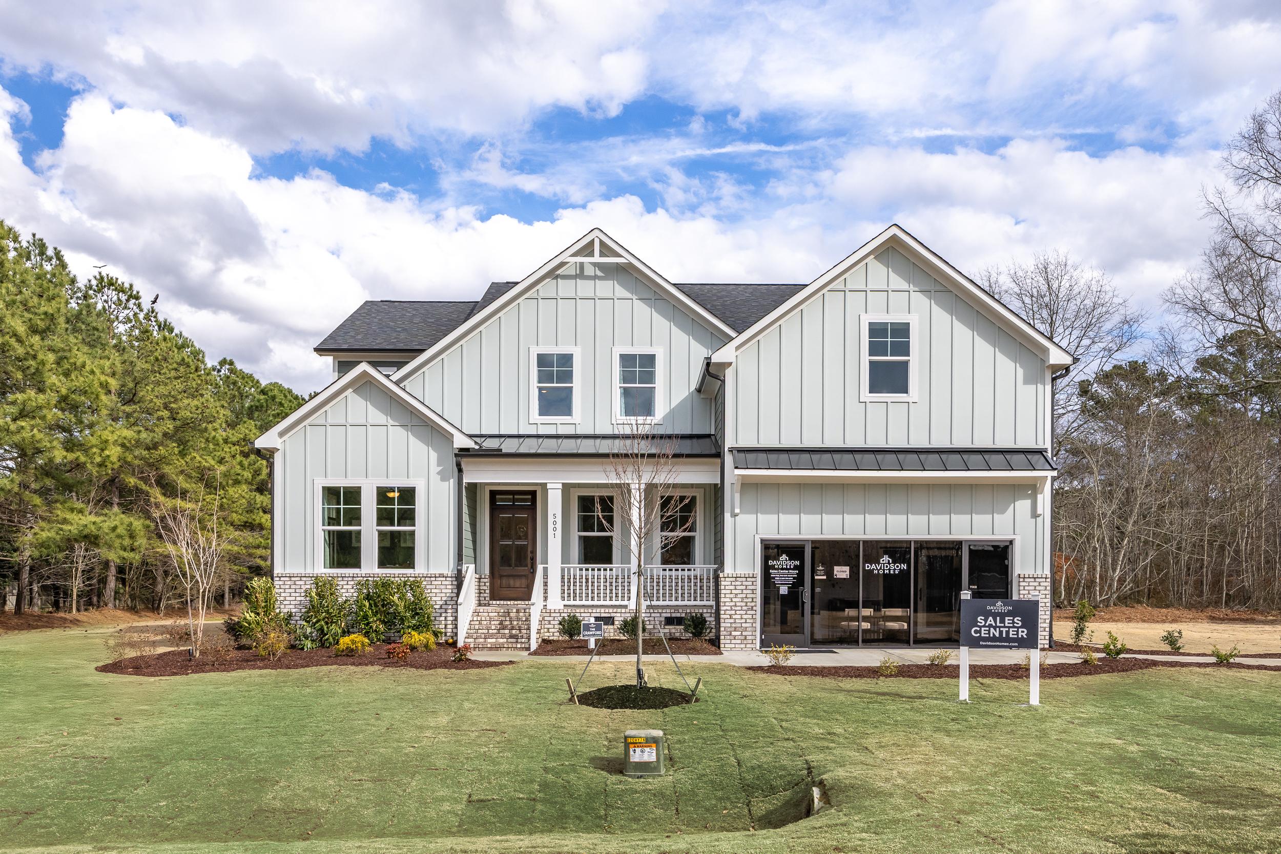 Modern farmhouse home exterior in Ashland, Apex NC with covered porch, white siding, and Davidson Homes sales center sign