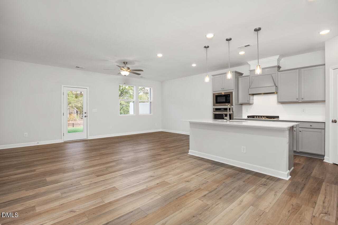 Open-concept kitchen-living area with gray cabinets, white island, pendant lights, ceiling fan, and French doors to backyard in Davidson Homes The Warren, Fuquay-Varina, NC