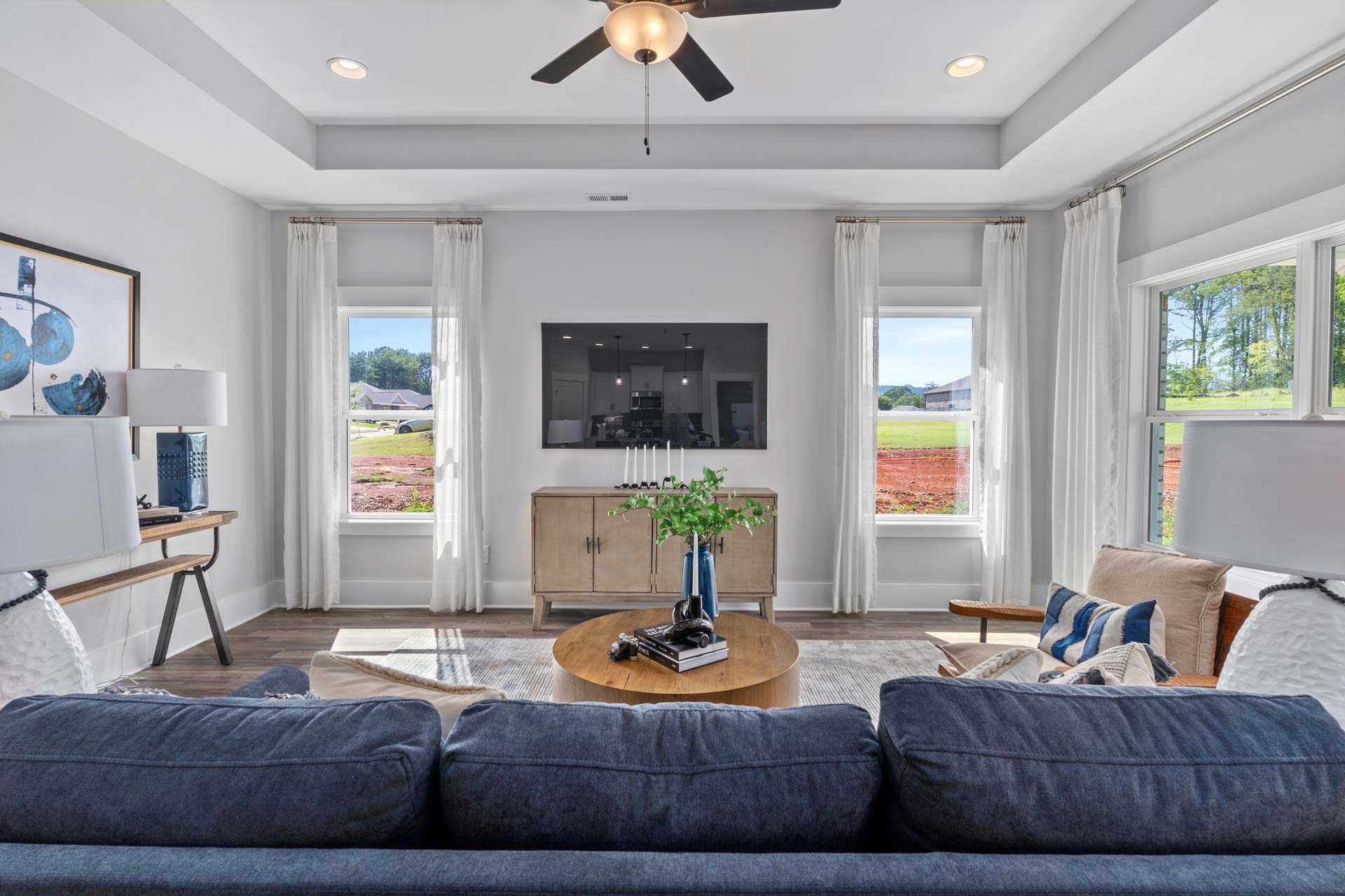 Modern living room in Blue Spring Huntsville AL with blue sectional sofa, mounted TV, large windows, and scenic outdoor view