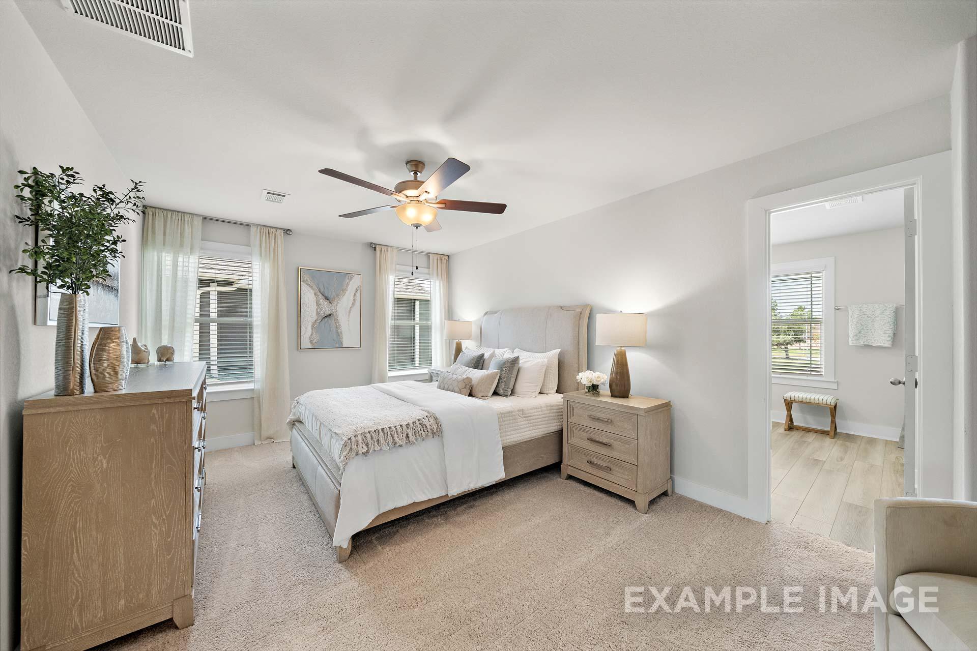 Spacious master bedroom in The Lily A home design featuring king bed, neutral tones, ceiling fan, and large windows