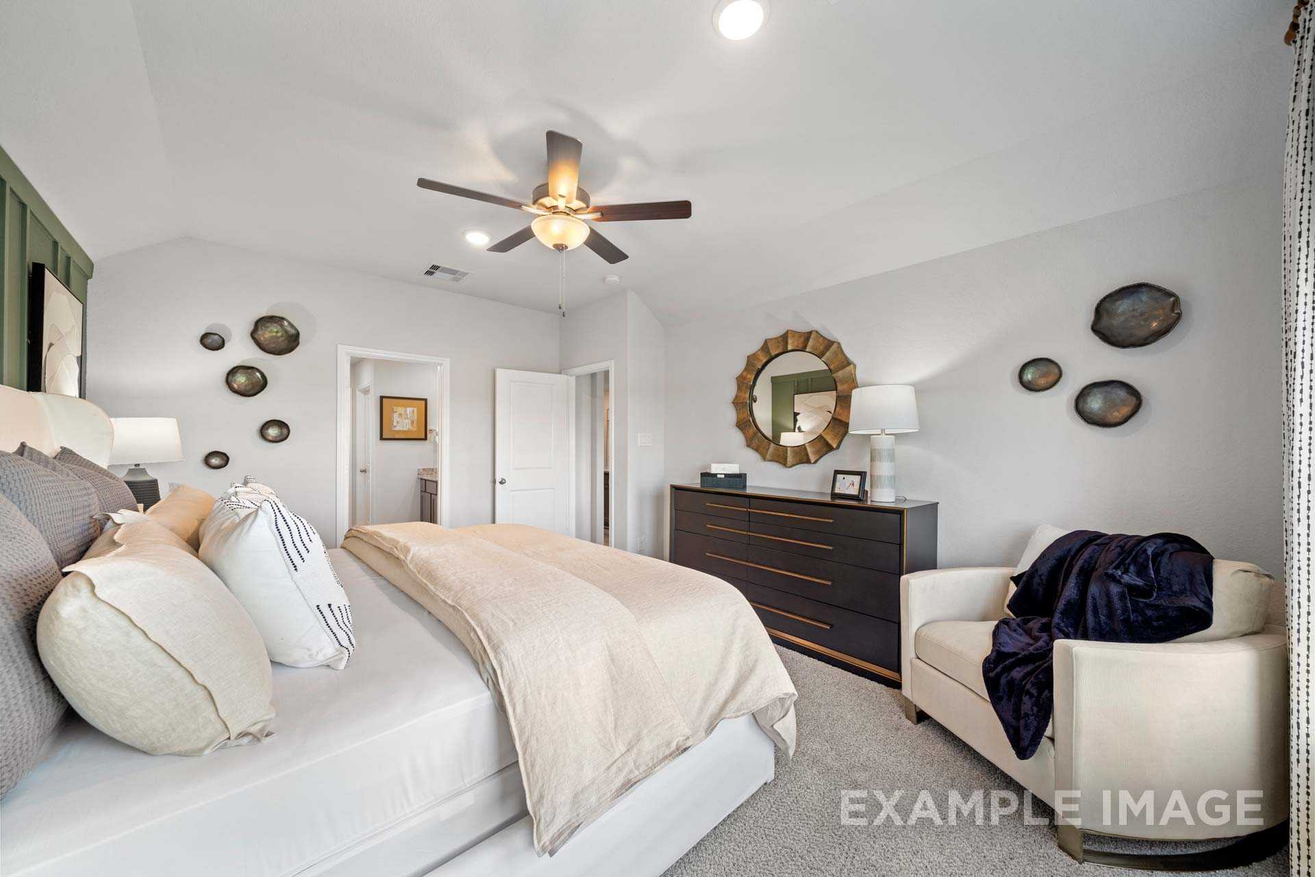 Spacious master bedroom in The Acadia B with king bed, neutral bedding, ceiling fan, round mirror, and accent chair