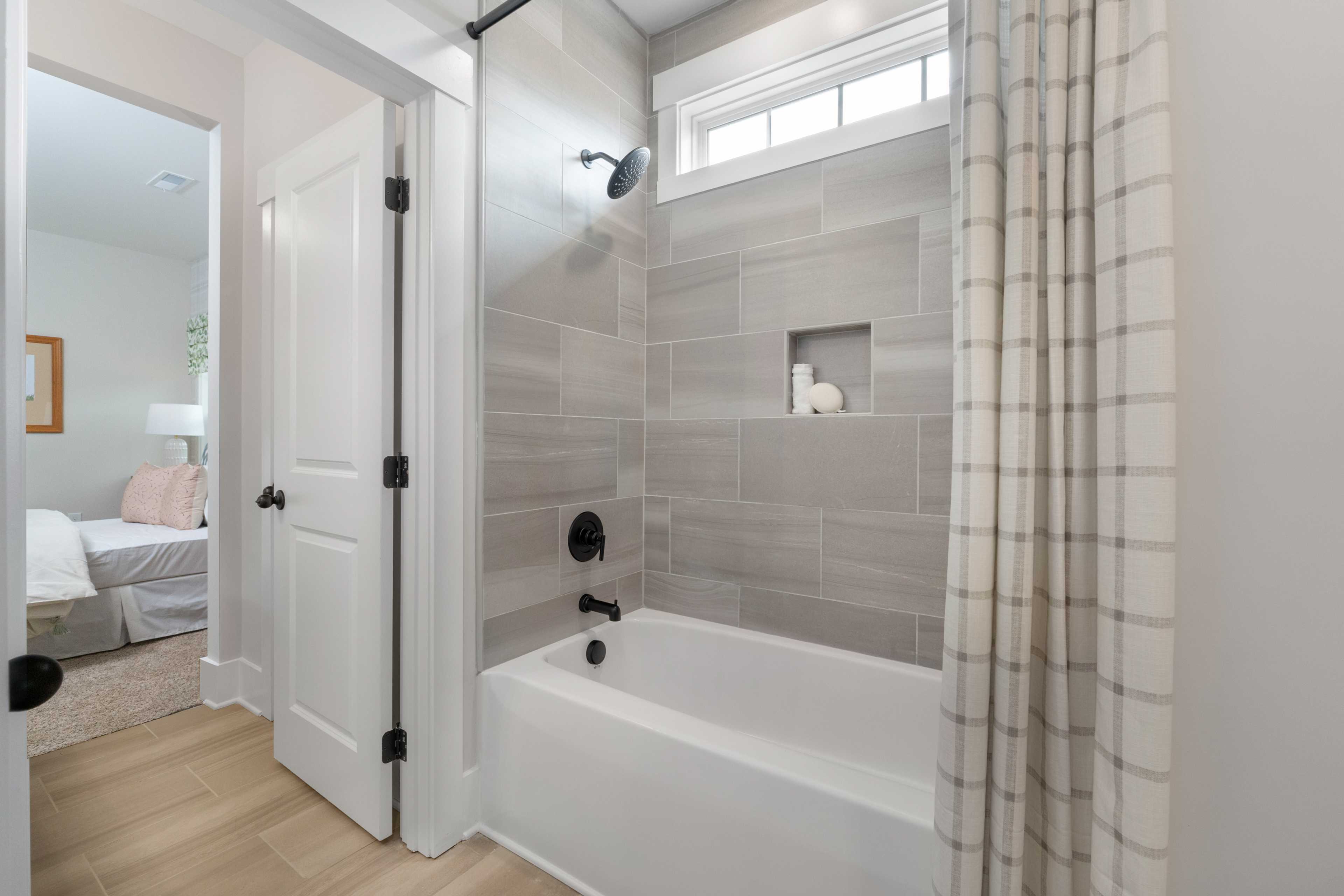 Spacious bathroom at Briercreek in Meridianville AL with white tub, gray tile shower, plaid curtain, and hardwood floors