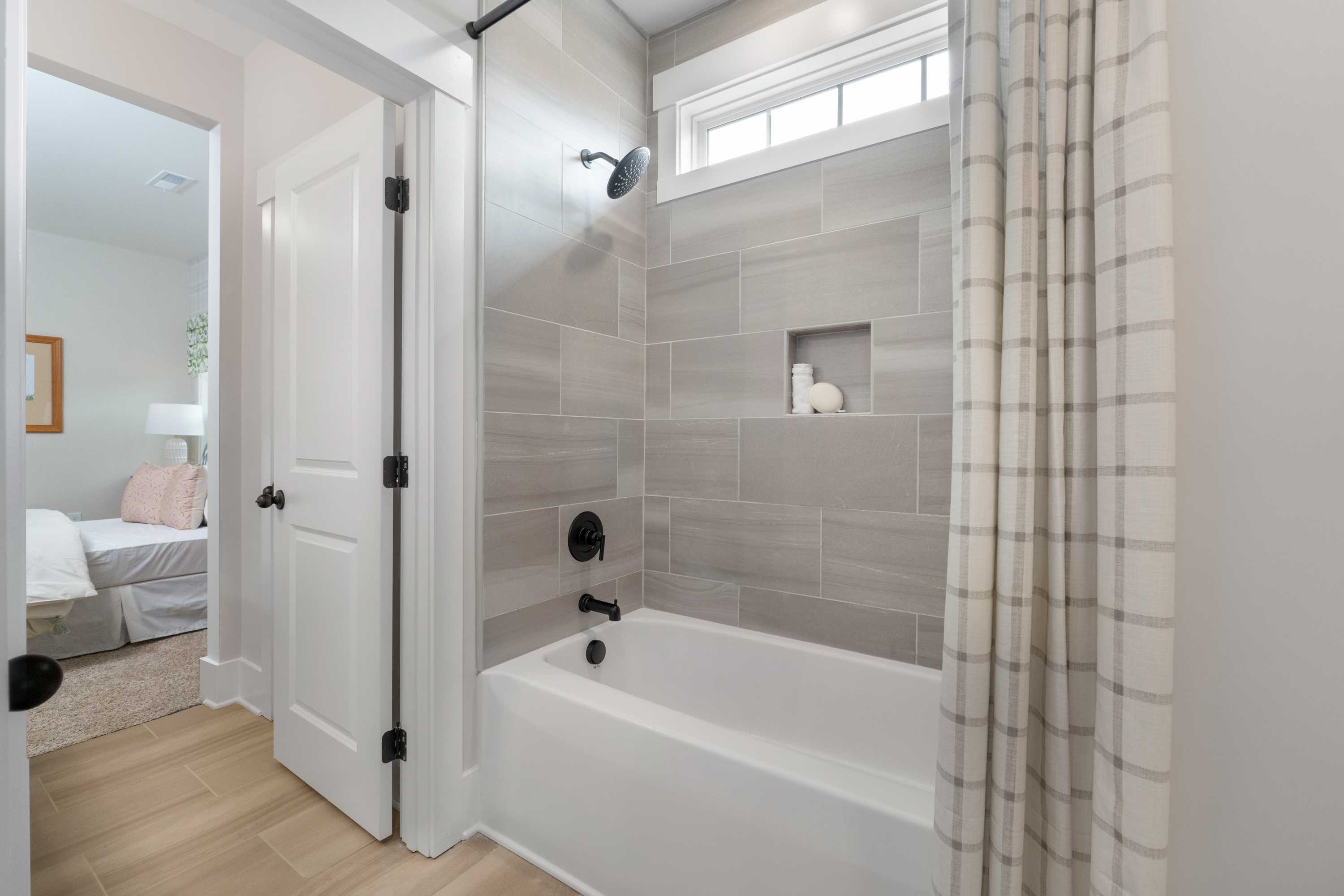 Spacious bathroom at Briercreek in Meridianville AL with white tub, gray tile shower, plaid curtain, and hardwood floors