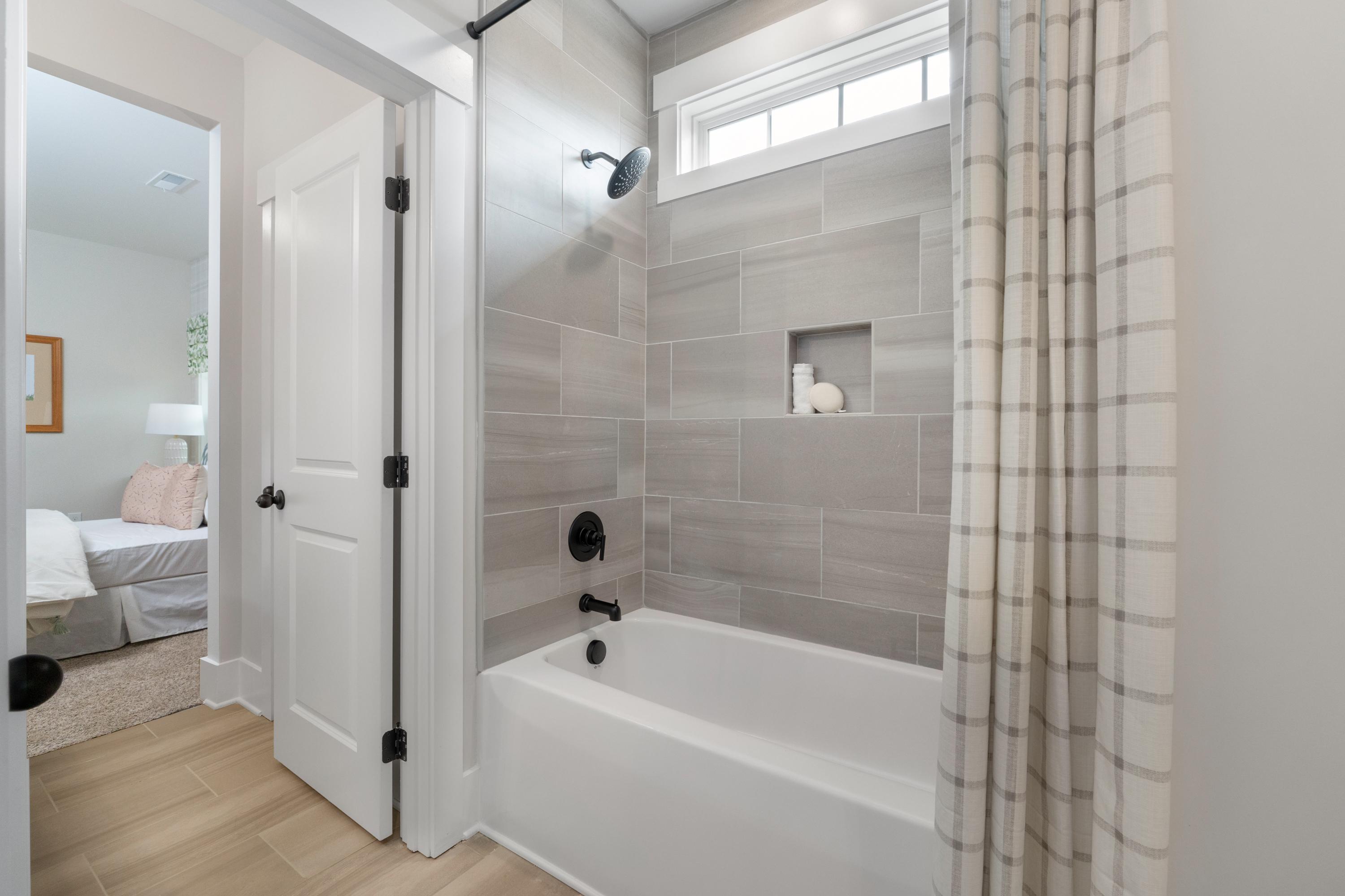 Spacious bathroom at Briercreek in Meridianville AL with white tub, gray tile shower, plaid curtain, and hardwood floors