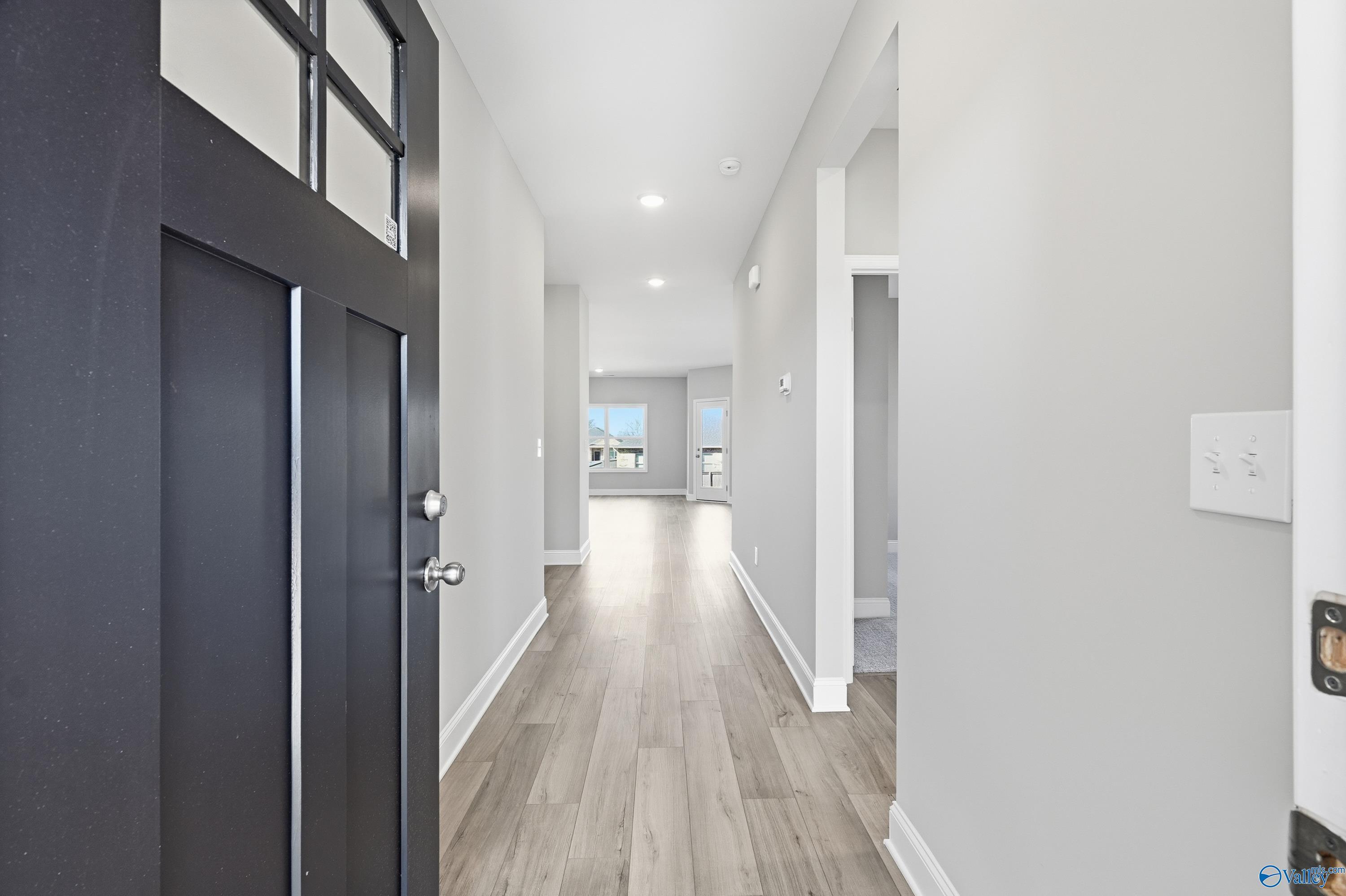 Spacious entry hallway with open black door, light oak floors, and recessed lights in Davidson Homes The Franklin C, New Market, Alabama