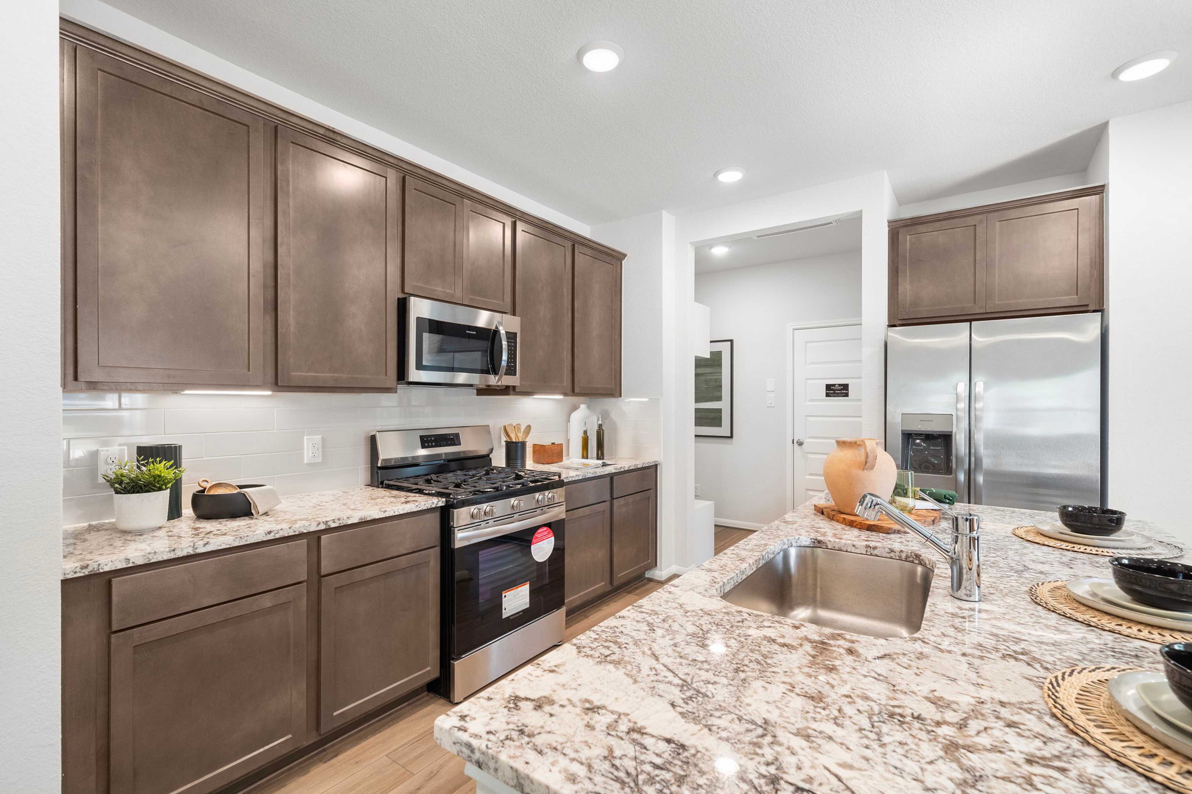 Spacious modern kitchen at Caney Creek Place in Conroe Texas with shaker brown cabinets stainless steel appliances and granite island