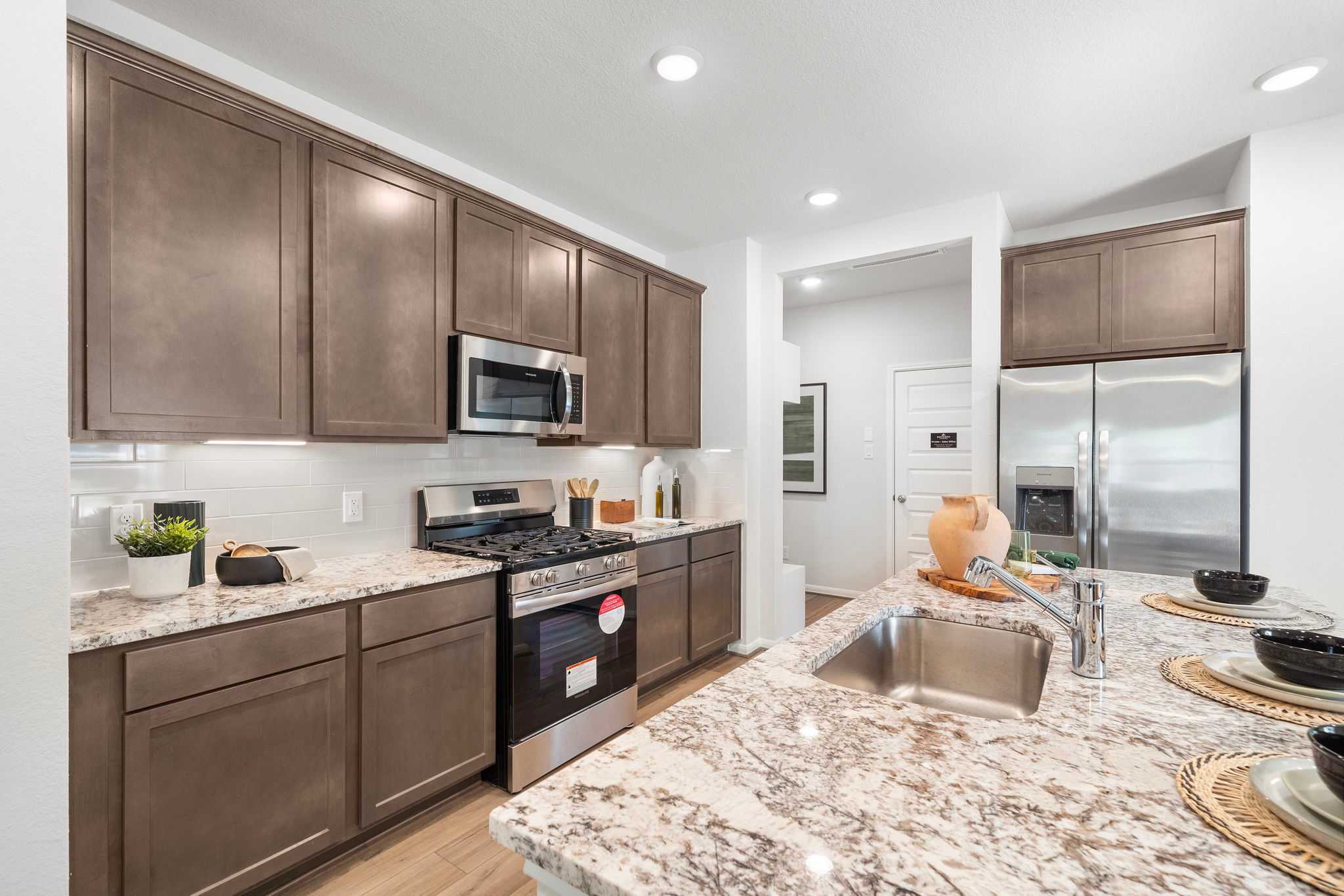 Spacious modern kitchen at Caney Creek Place in Conroe Texas with shaker brown cabinets stainless steel appliances and granite island