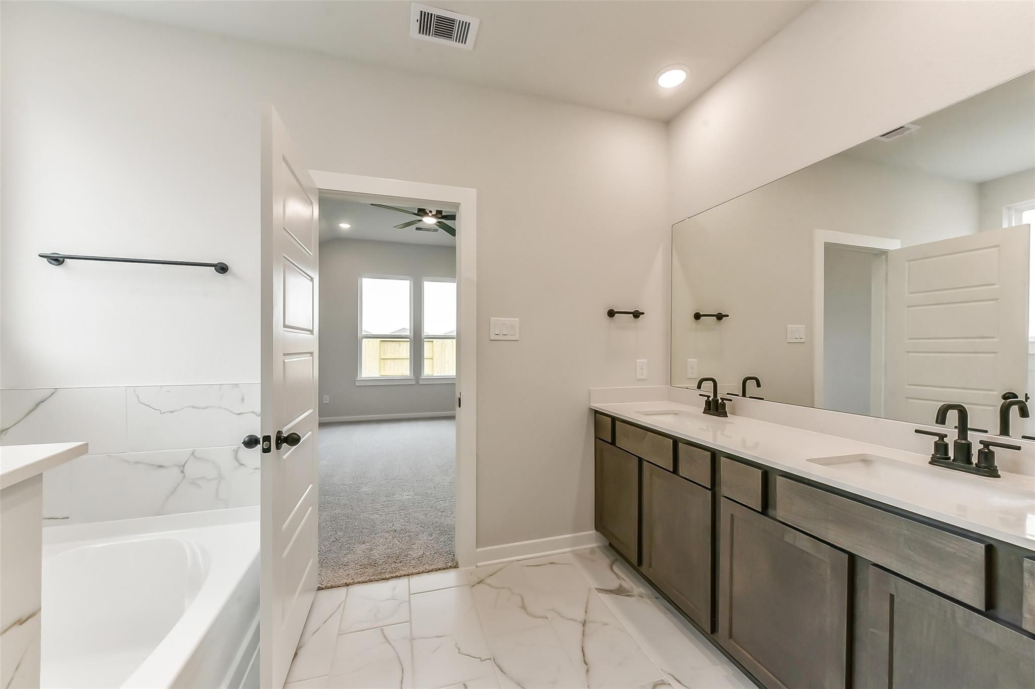 Elegant master bathroom featuring double vanity with quartz counters, marble-look tiles, freestanding tub in Davidson Homes Sequoia C, Crosby TX