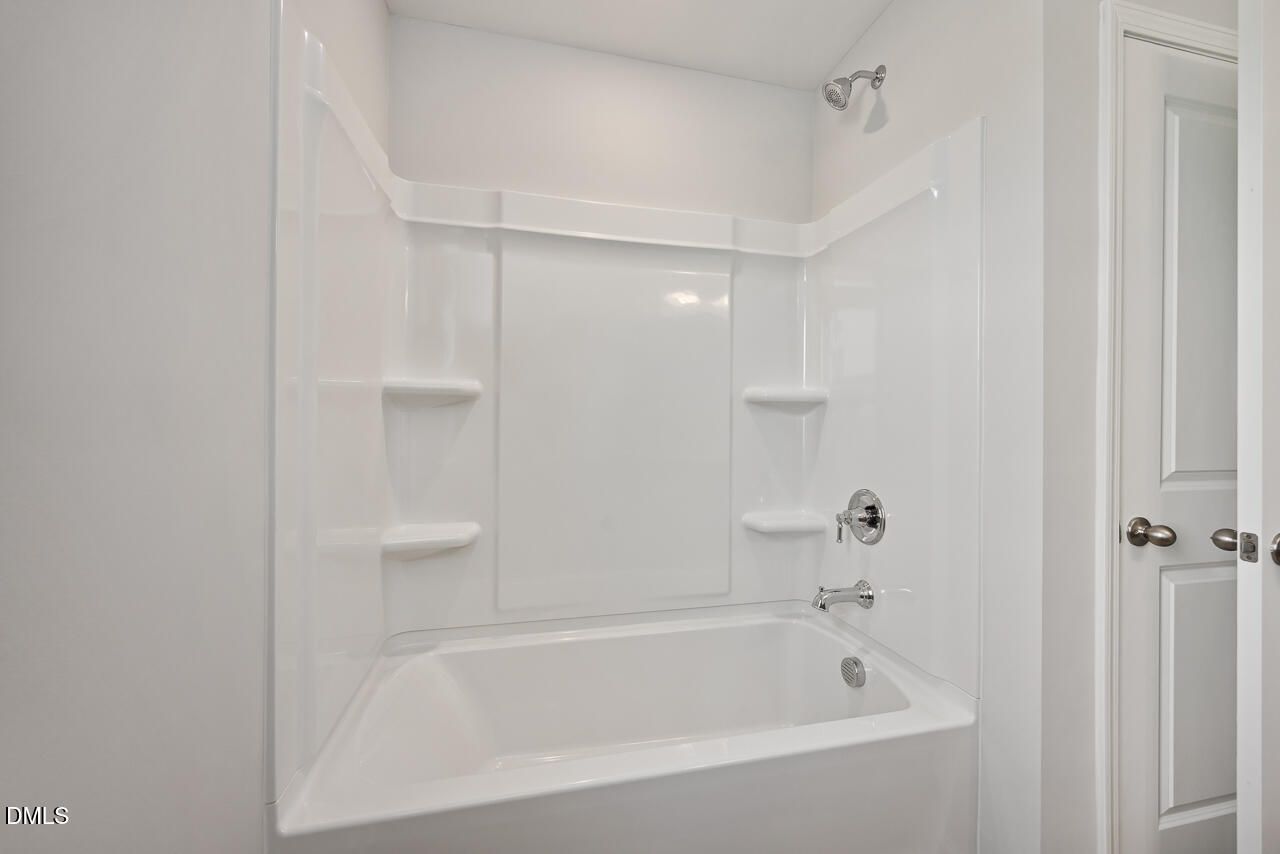 White bathtub-shower combo with chrome fixtures and built-in shelves in Davidson Homes The Willow G, Angier, NC