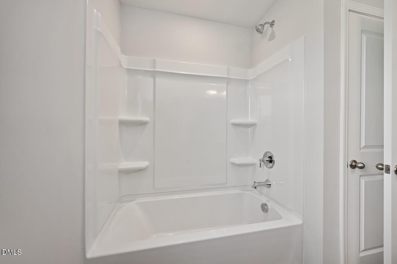 White bathtub-shower combo with chrome fixtures and built-in shelves in Davidson Homes The Willow G, Angier, NC