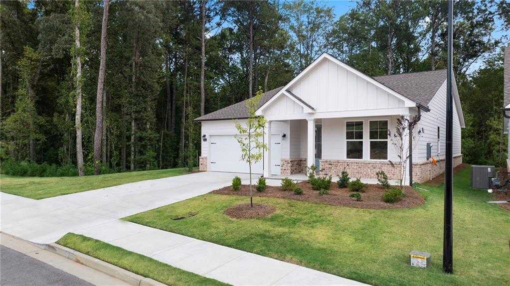 Modern white single-story 4-bedroom home with 2-car garage, front porch, and wooded yard in Kelly Preserve, Loganville, Georgia