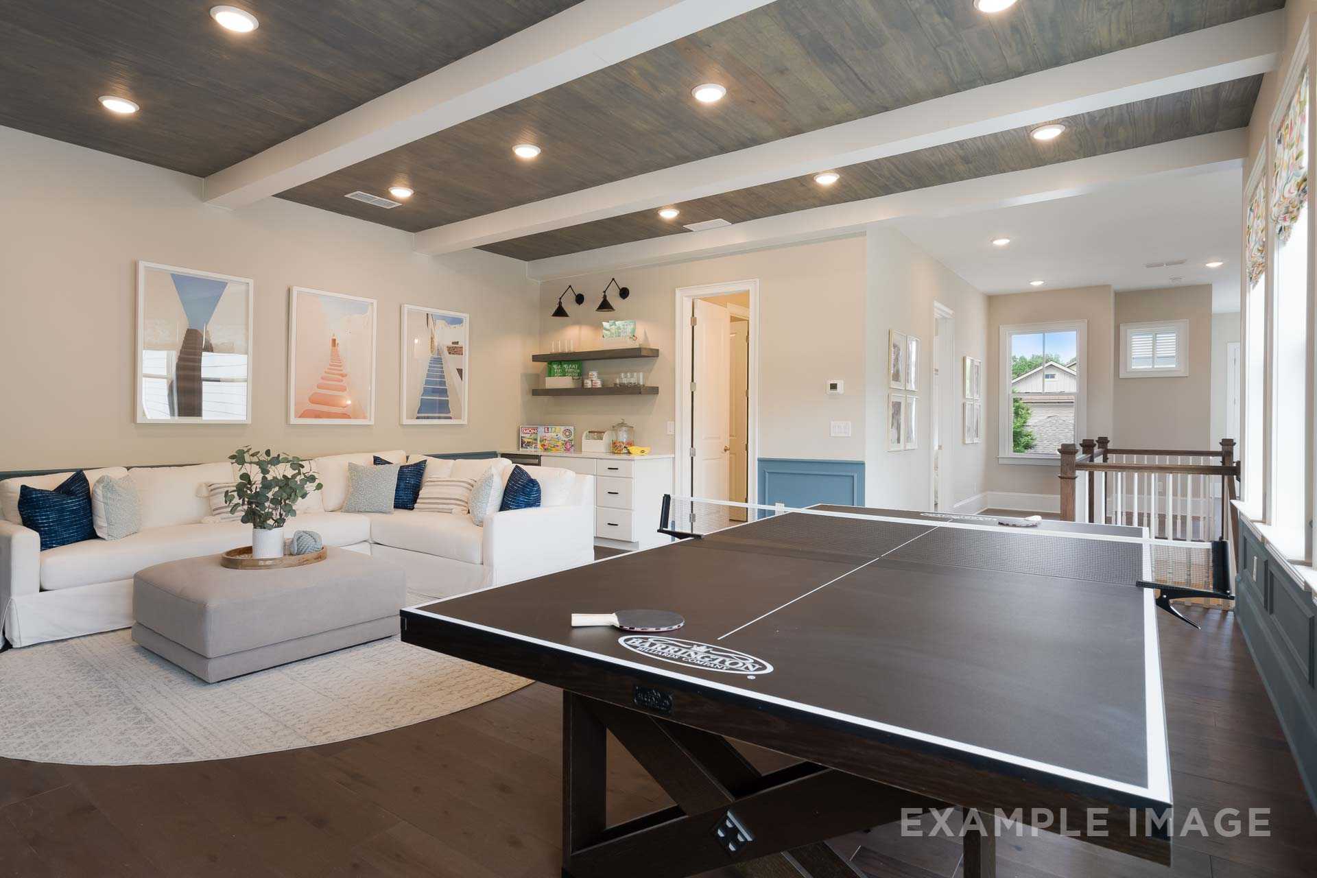 Spacious upper-floor game room in The Seaside Davidson Homes design featuring ping pong table, white sectional sofa, and beamed ceiling