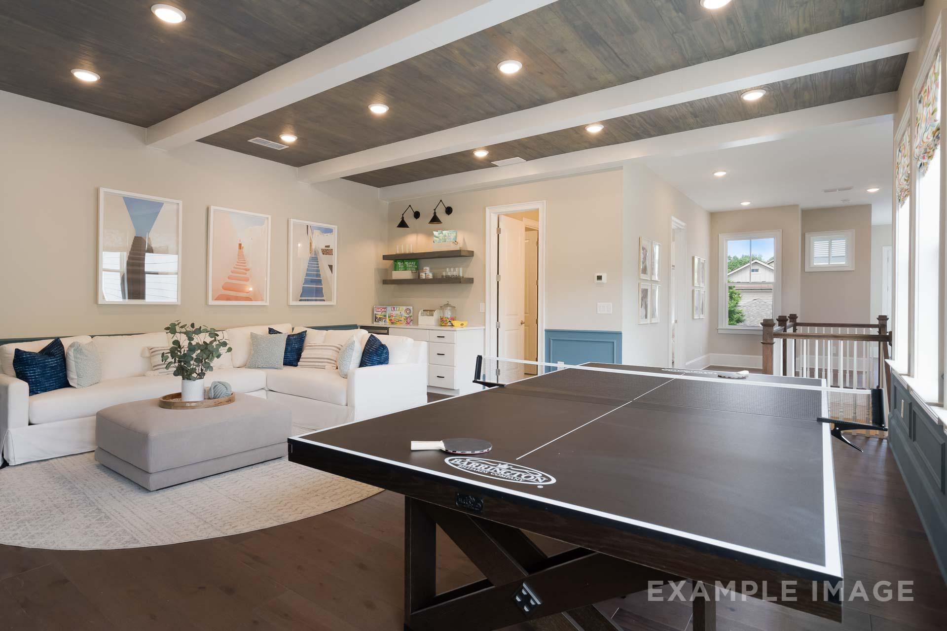 Spacious bonus room in The Seaside C home design with ping pong table, white sofa, coastal art, and beamed ceiling