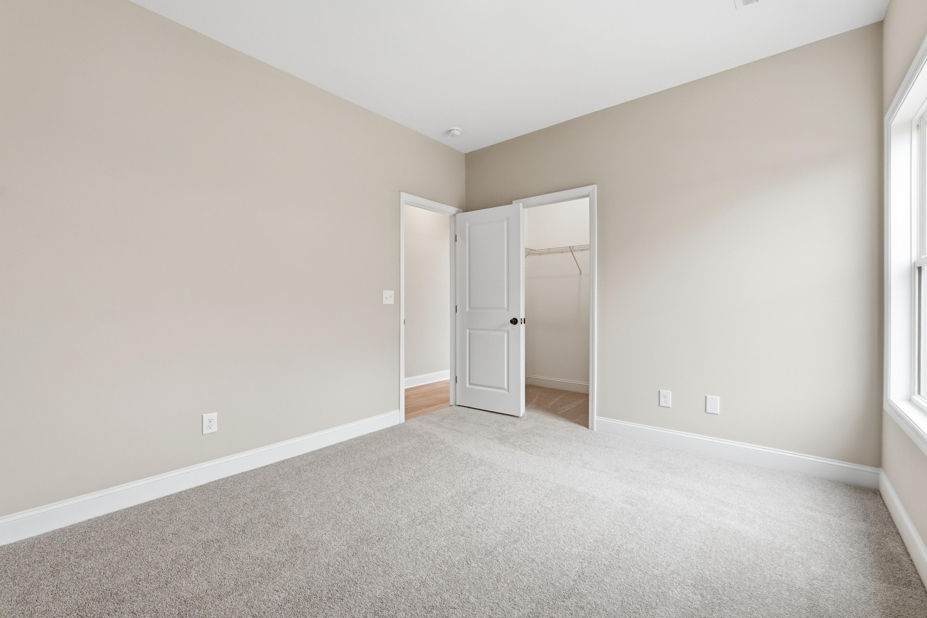 Spacious master bedroom in The Rockford home design by Davidson Homes featuring beige walls, carpet flooring, and walk-in closet