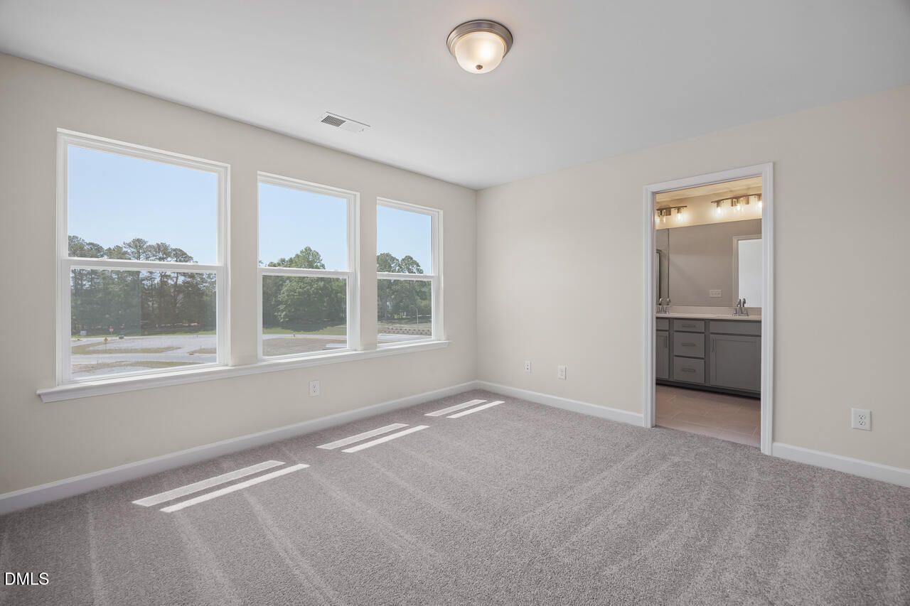 Bright bedroom with plush carpet and en-suite bathroom in The Mitchell floor plan at Camden Park, Knightdale, NC.