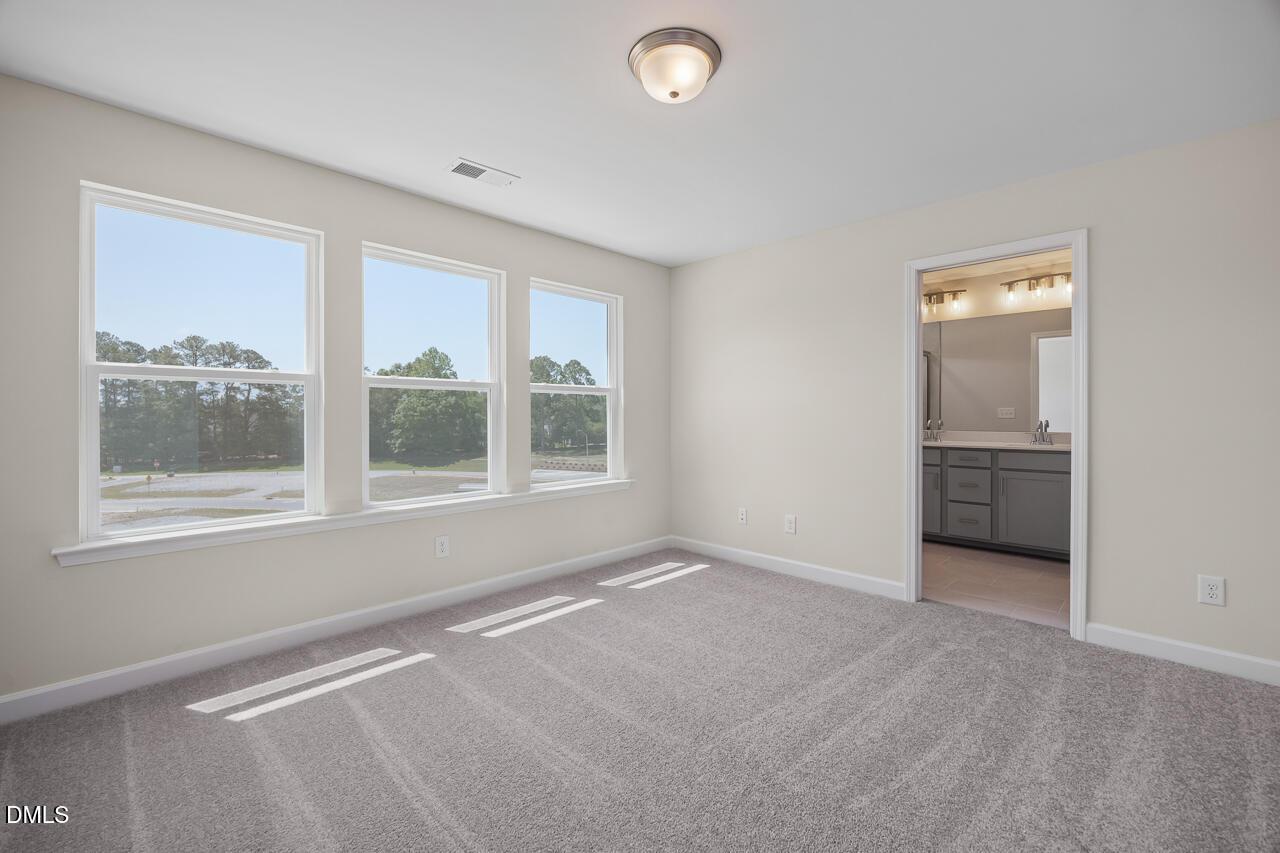 Bright bedroom with plush carpet and en-suite bathroom in The Mitchell floor plan at Camden Park, Knightdale, NC.