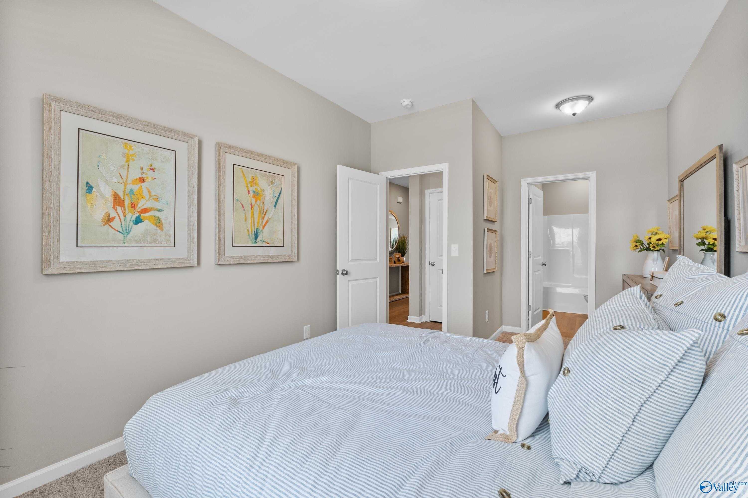 Cozy bedroom with blue striped bedding, yellow floral artwork, and en-suite bath in Davidson Homes The Sanctuary, Athens, Alabama