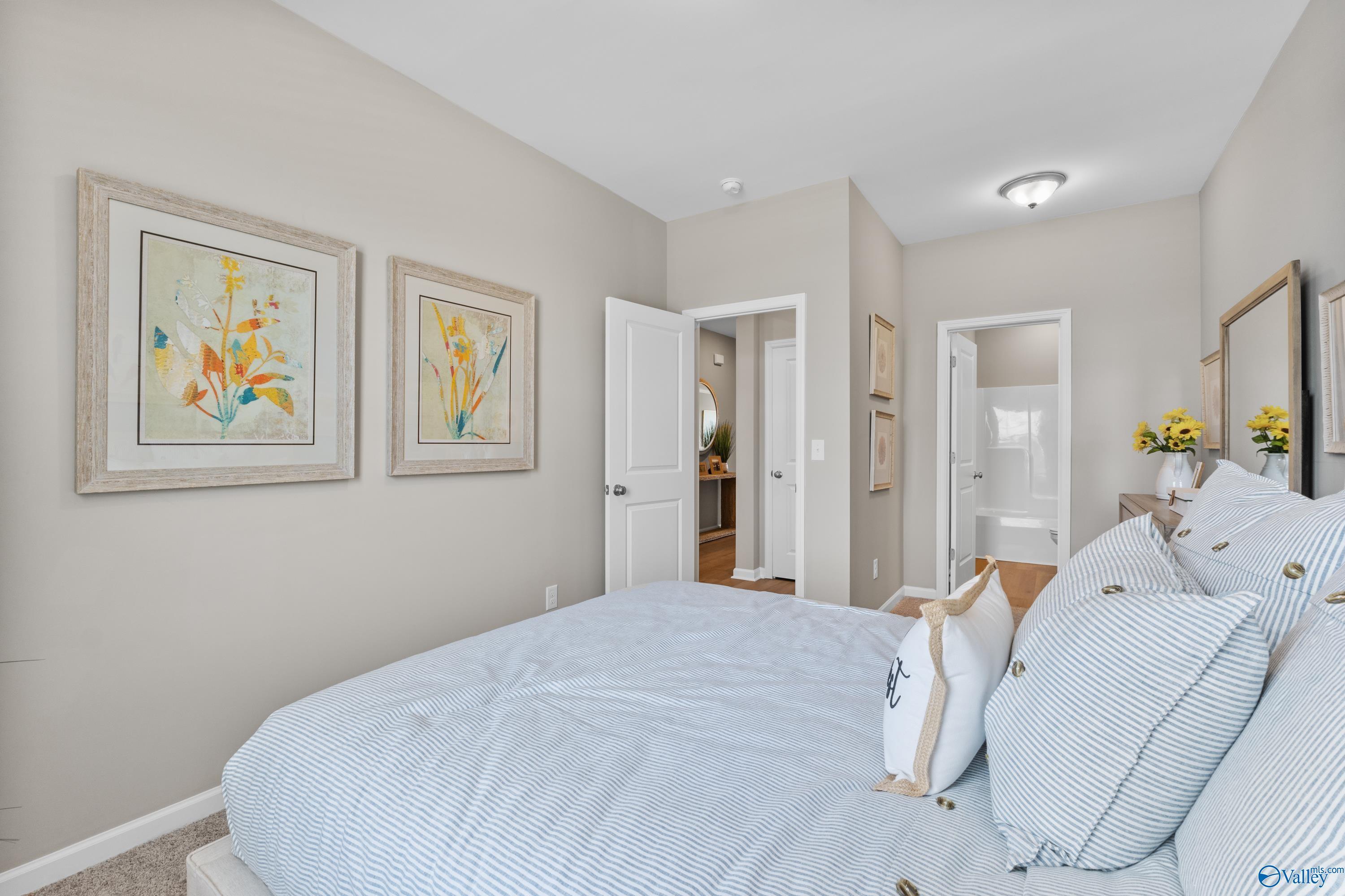 Cozy bedroom with blue striped bedding, yellow floral artwork, and en-suite bath in Davidson Homes The Sanctuary, Athens, Alabama