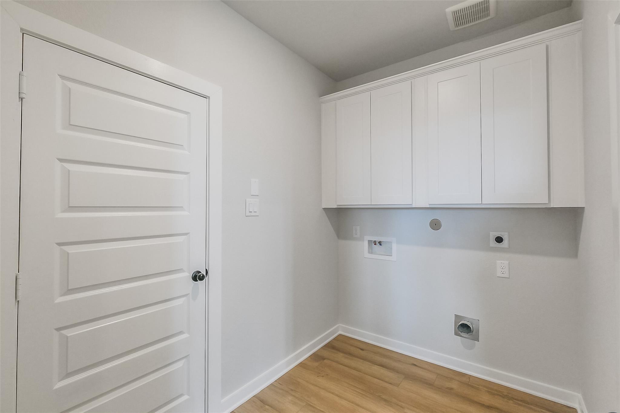 Modern laundry room with white shaker cabinets, washer-dryer hookups, and hardwood floors in Davidson Homes Tierra B, Beasley, TX