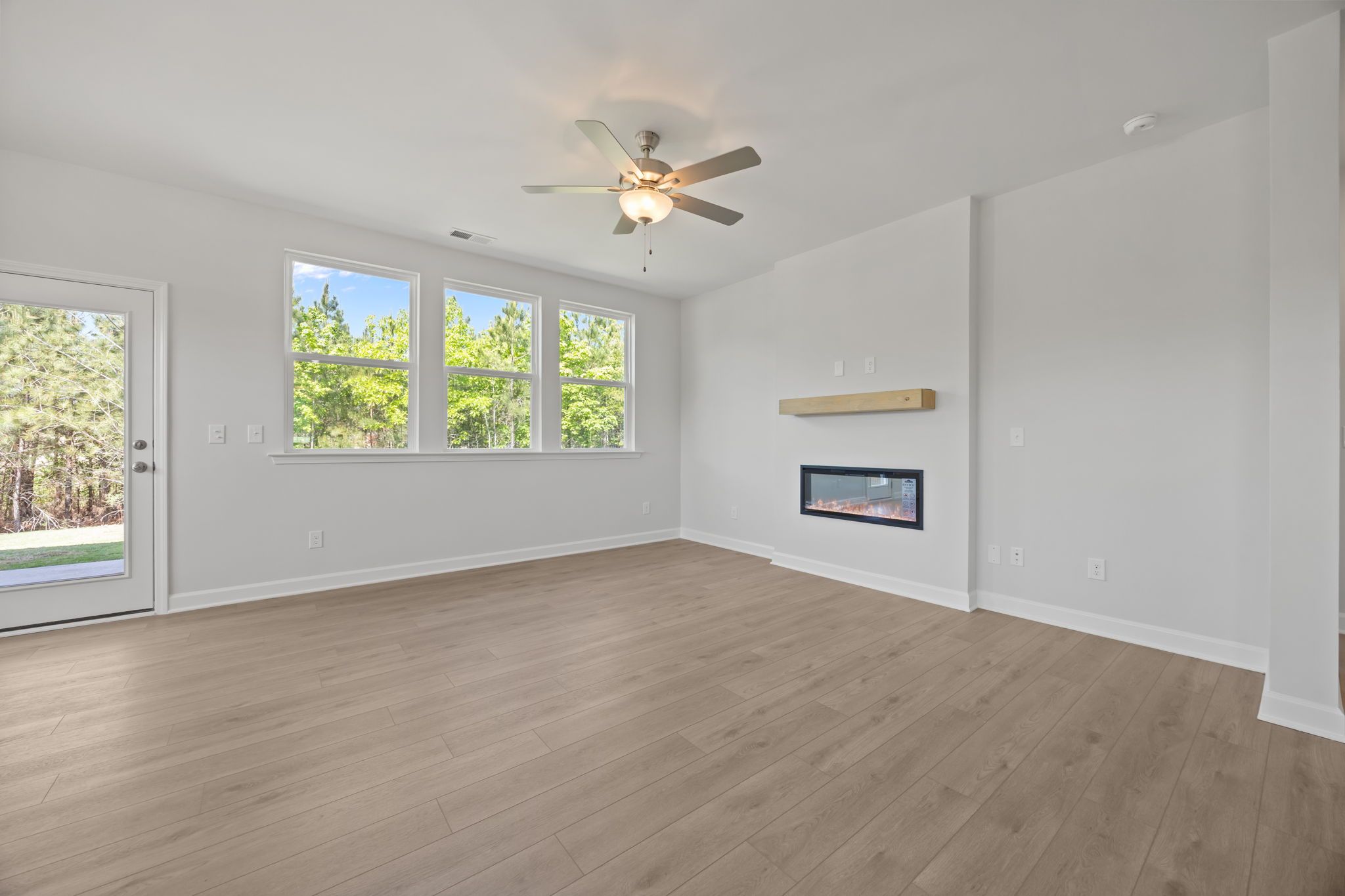 Spacious living area in The Ashport B featuring a modern linear fireplace, wood flooring, and large windows.