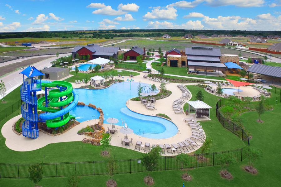 Resort-style swimming pool with twisting green waterslide at Heartland Texas community by Davidson Homes, lounge seating and cabanas