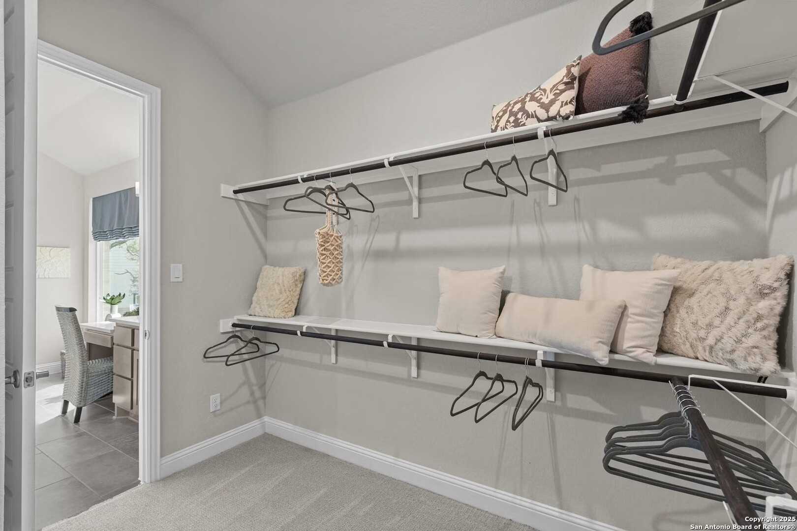 Spacious walk-in closet with built-in shelves, hanging rods, and neutral decor in The Garner A by Davidson Homes, Castroville, Texas