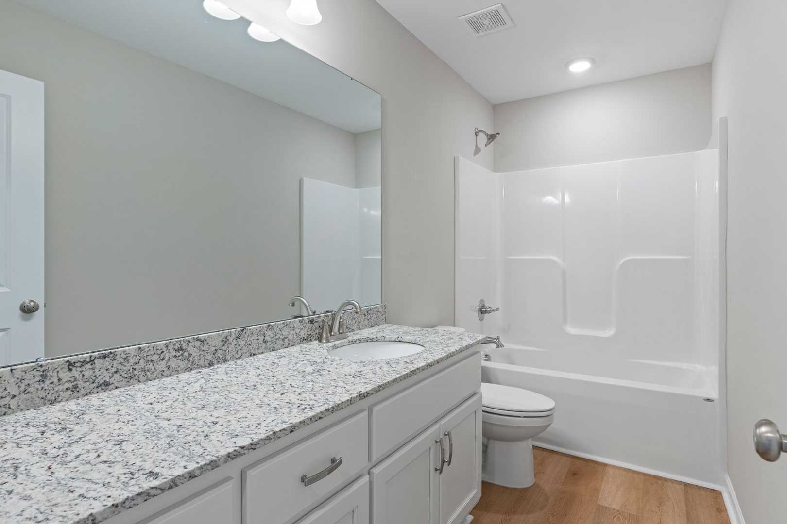 Spacious secondary bathroom in The Stella with granite vanity, white tub, shower and neutral tones by Evermore Homes