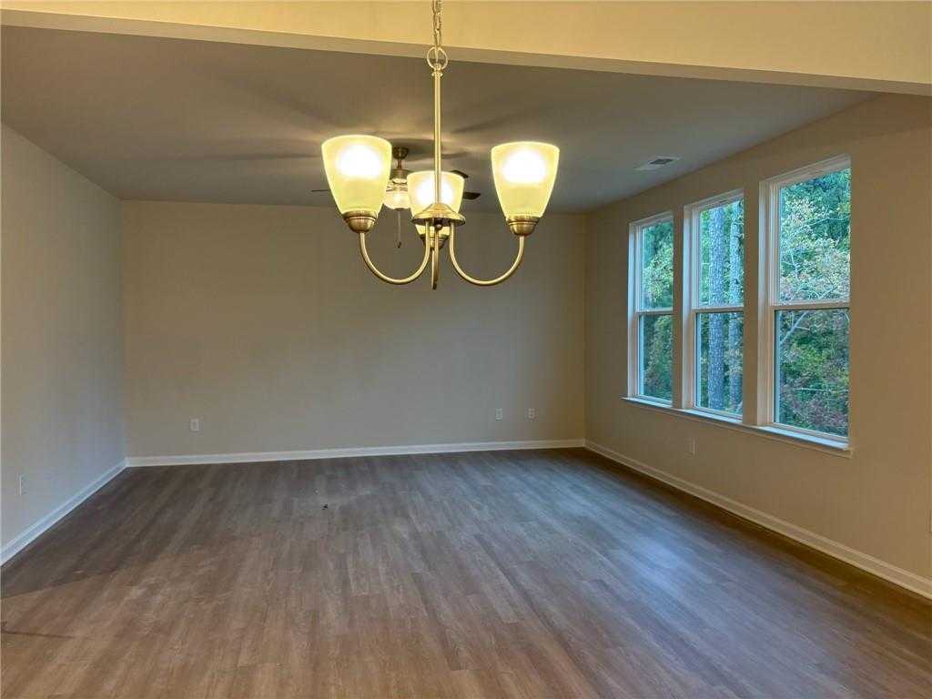 Bright living room with hardwood floors, elegant chandelier, and large windows overlooking trees in Davidson Homes The Hickory A, Dallas, Georgia