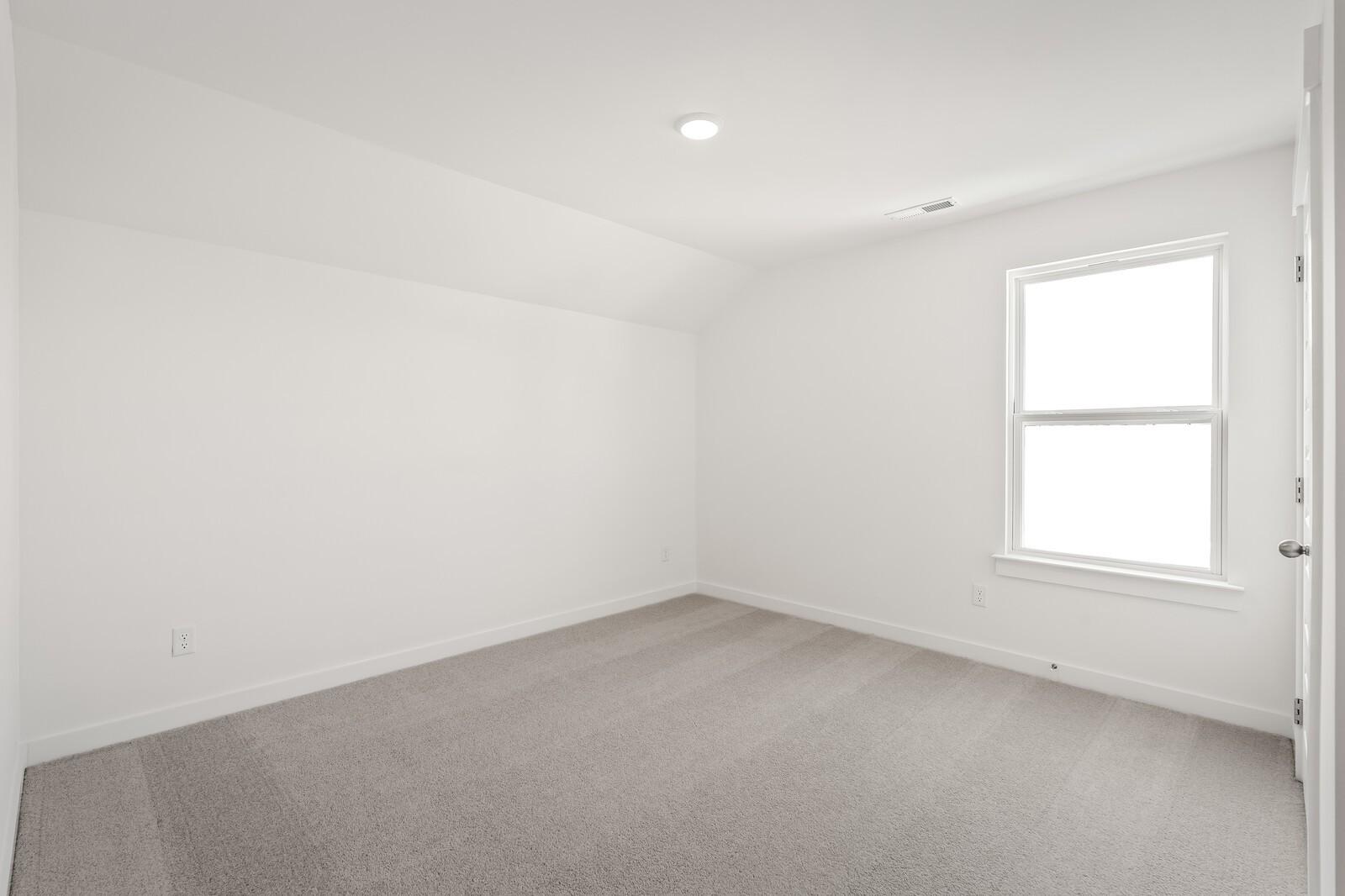 Bright empty bedroom with white walls, gray carpet, and large window in Davidson Homes The Ash A, Gallatin, TN