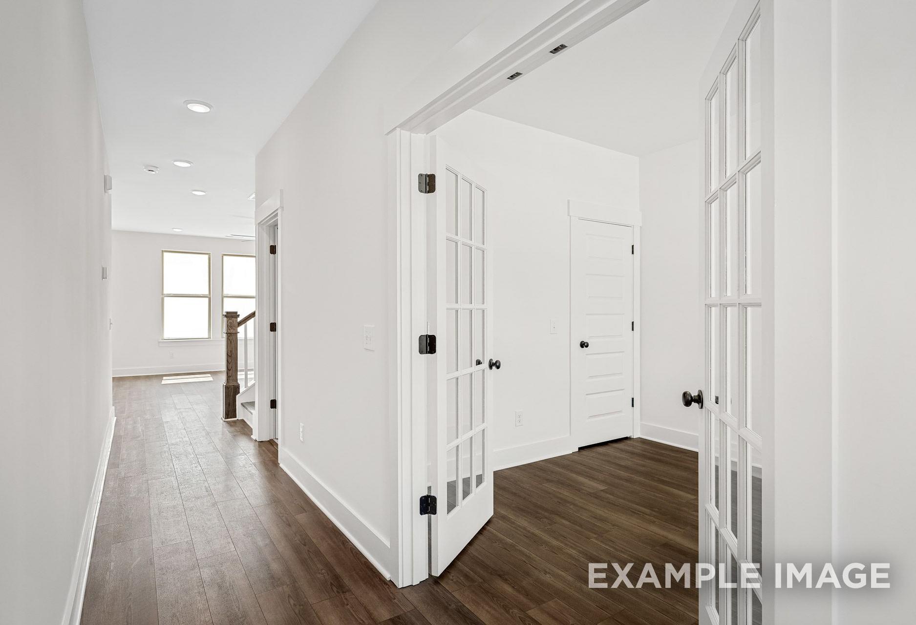 Spacious upper floor hallway in The Logan A home with French doors to master suite, hardwood floors, and white walls