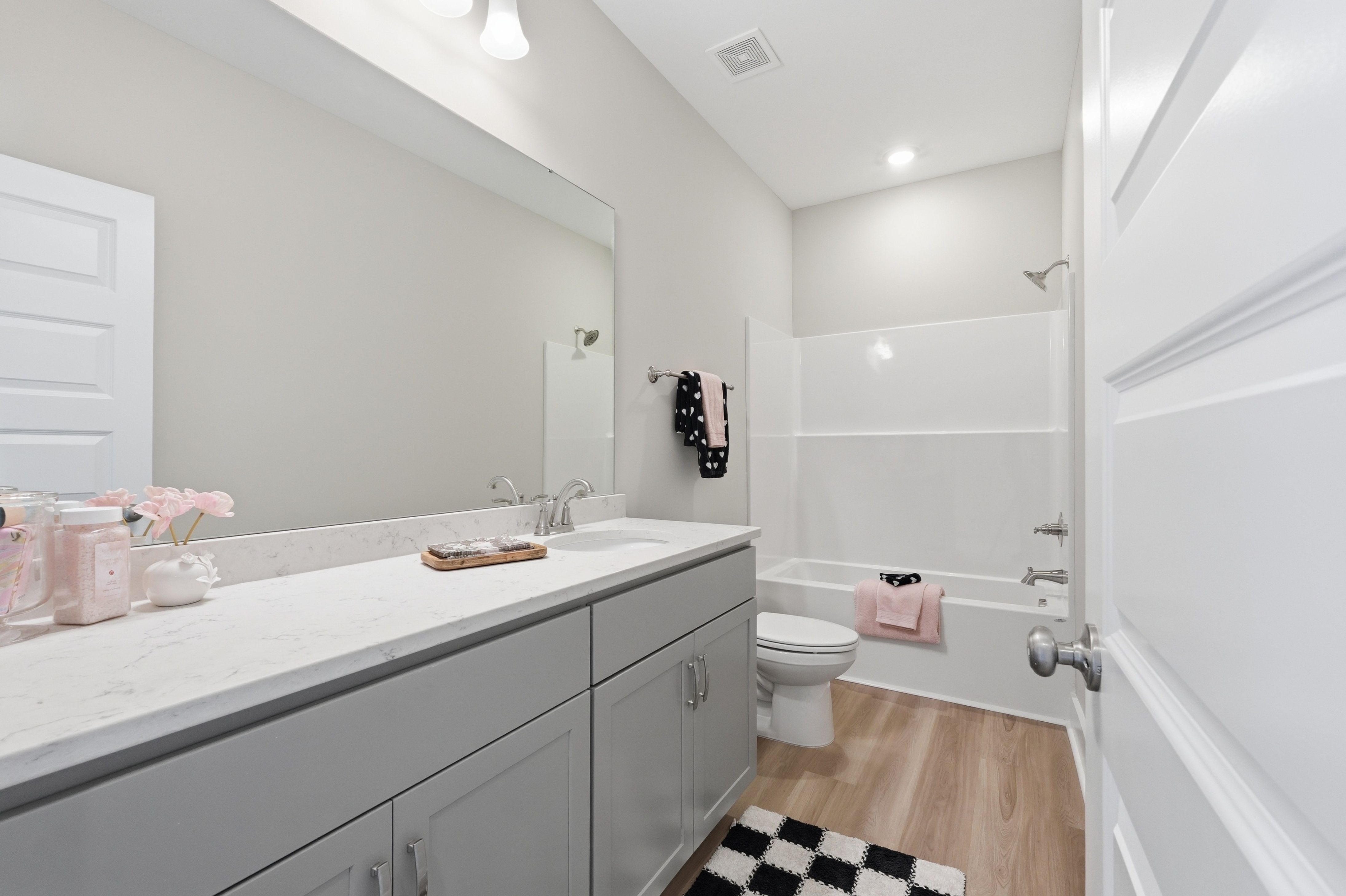 Spacious bathroom at The Meadows at Hampton Cove in Owens Cross Roads AL with gray vanity, white tub shower, large mirror, and pink accents