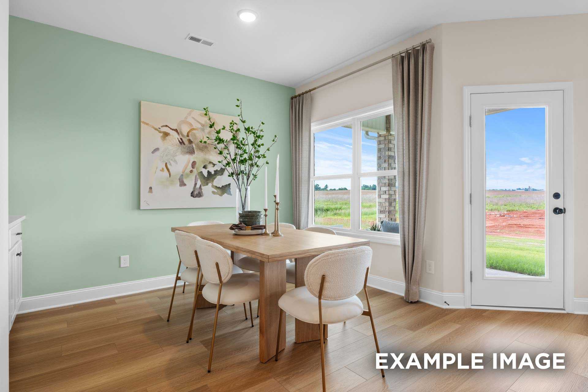 Bright dining room in The Laurel N home with green walls, wooden table, white chairs, abstract art, and large windows overlooking fields