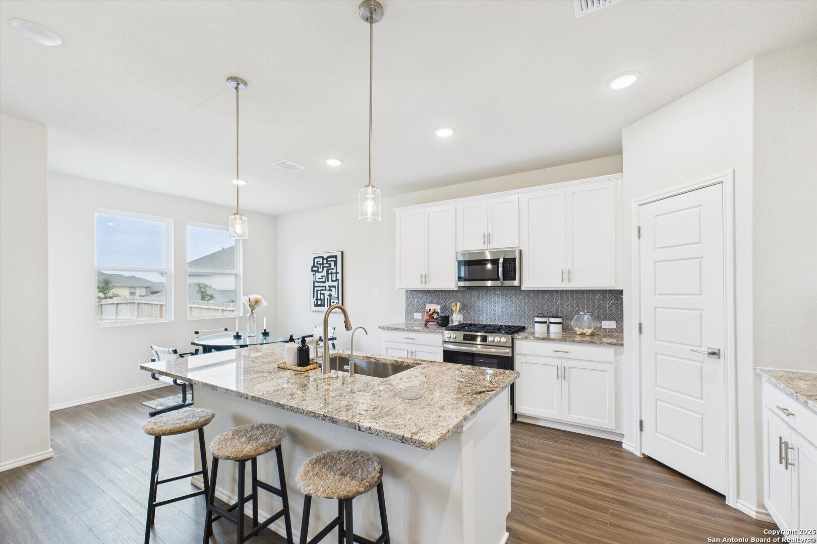 Bright modern kitchen with white cabinets, granite island, stainless appliances, pendant lights in Davidson Homes The Asheville K, Bricewood San Antonio
