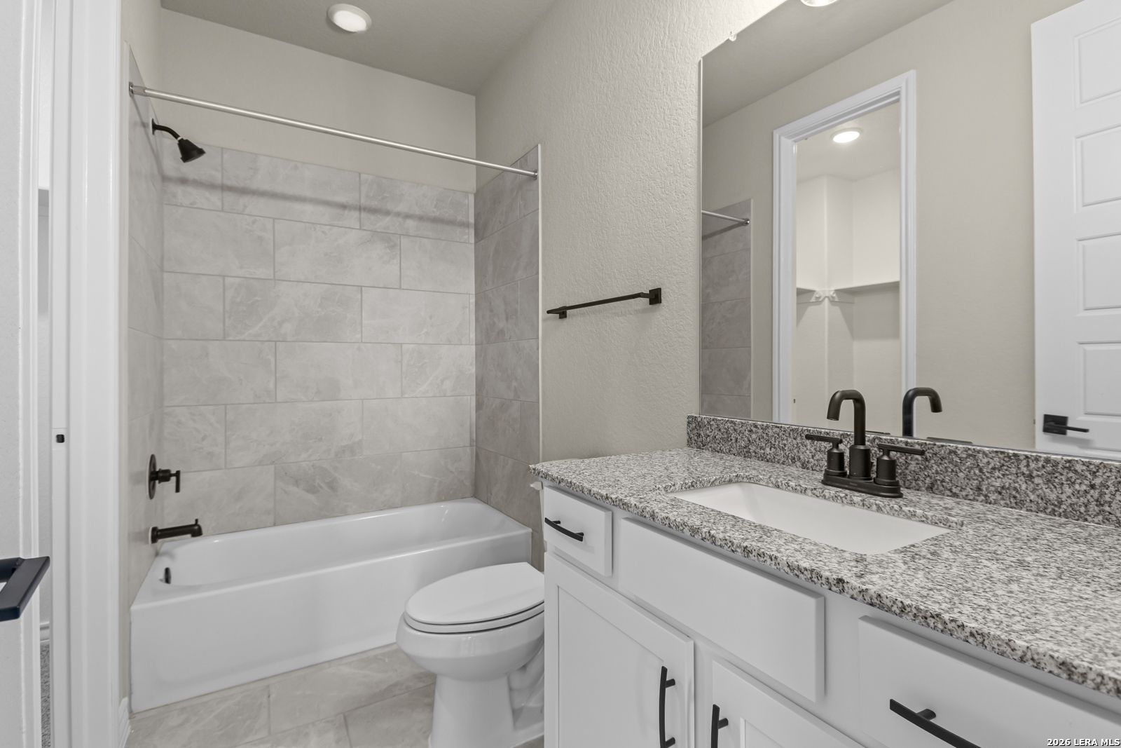 Modern bathroom with granite vanity, tiled tub-shower combo, and dark fixtures in The Danbury H home, Castroville, Texas.