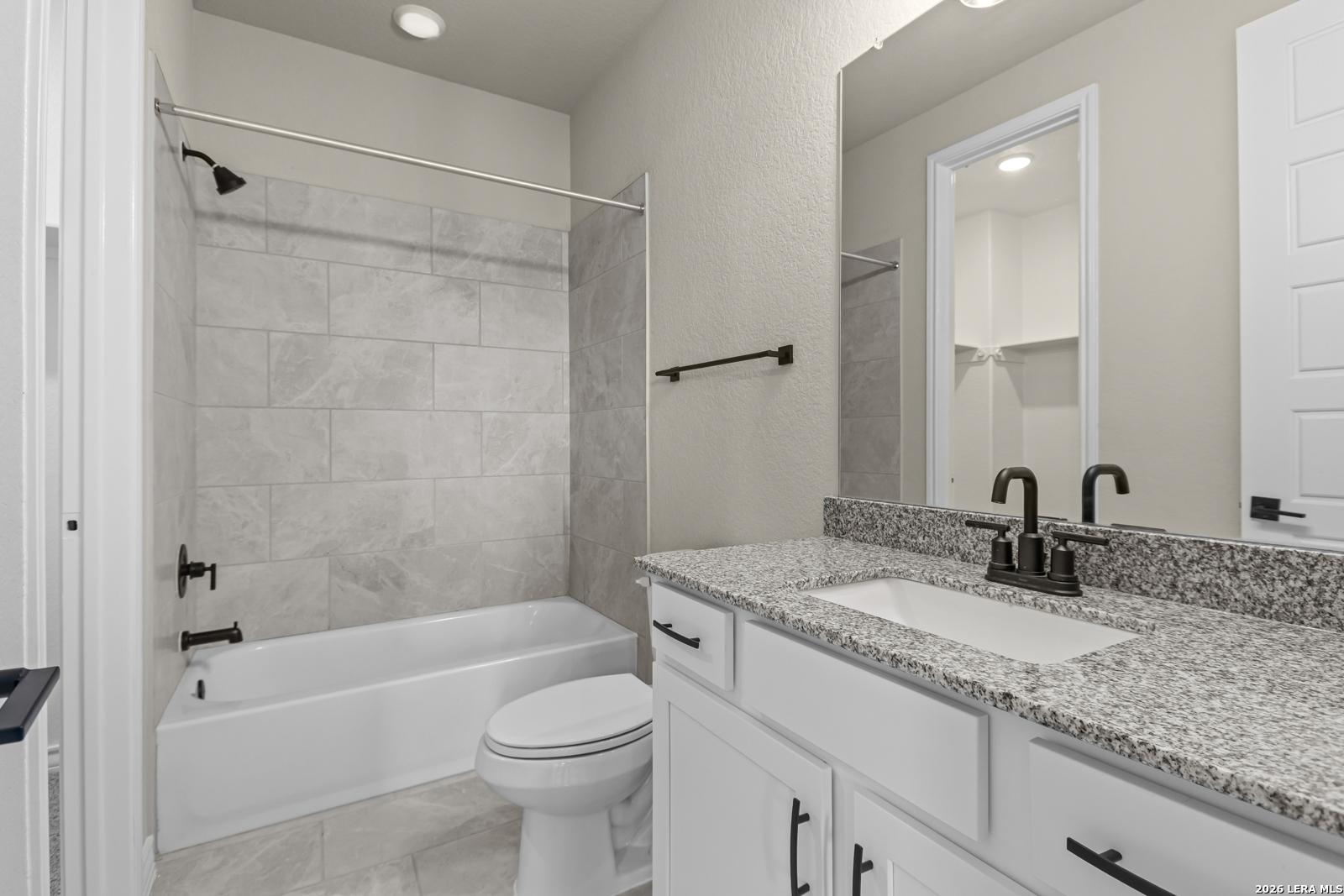 Modern bathroom with granite vanity, tiled tub-shower combo, and dark fixtures in The Danbury H home, Castroville, Texas.