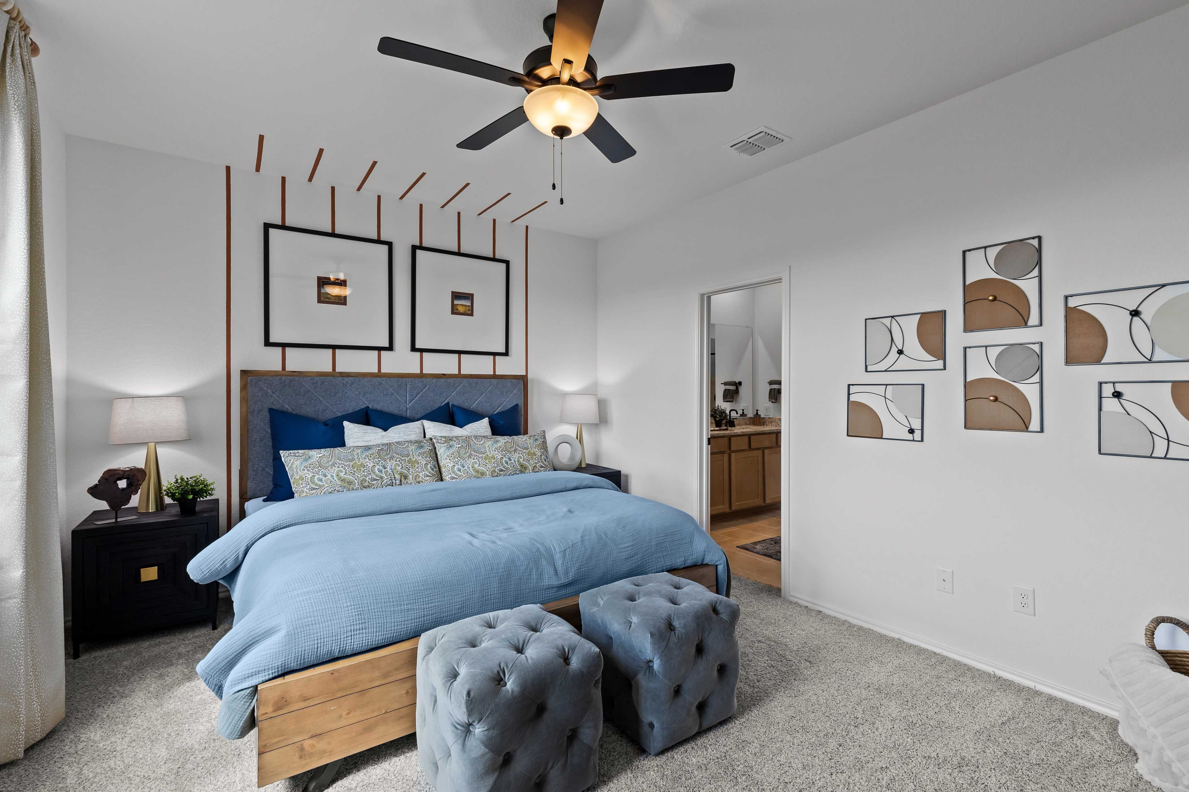 Spacious primary bedroom at Hickory Ridge in Elmendorf Texas with blue king bed, abstract wall art, and ceiling fan