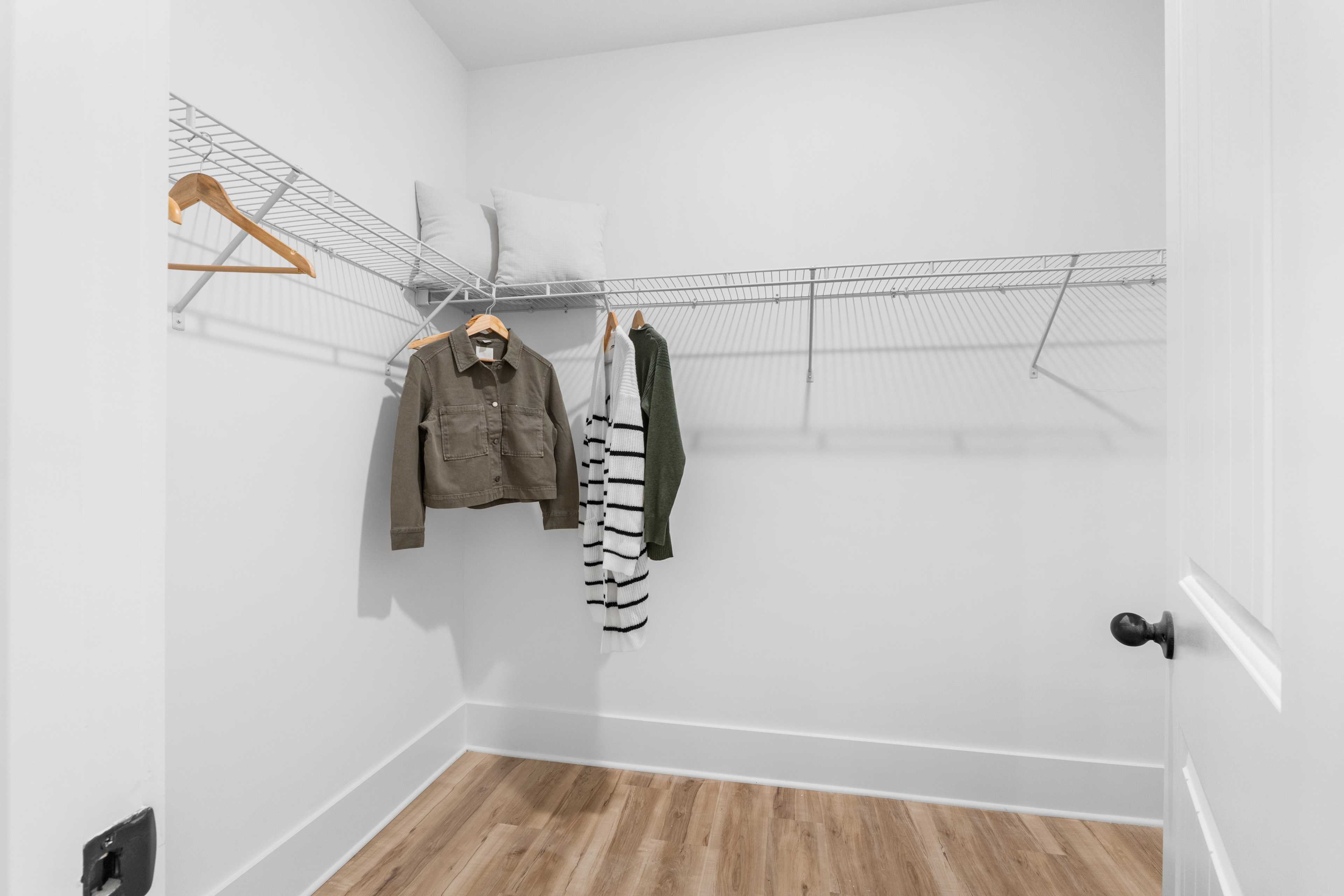 Spacious walk-in closet in Spragins Cove Huntsville AL with white walls, wire shelving, and hanging clothes on wooden hangers