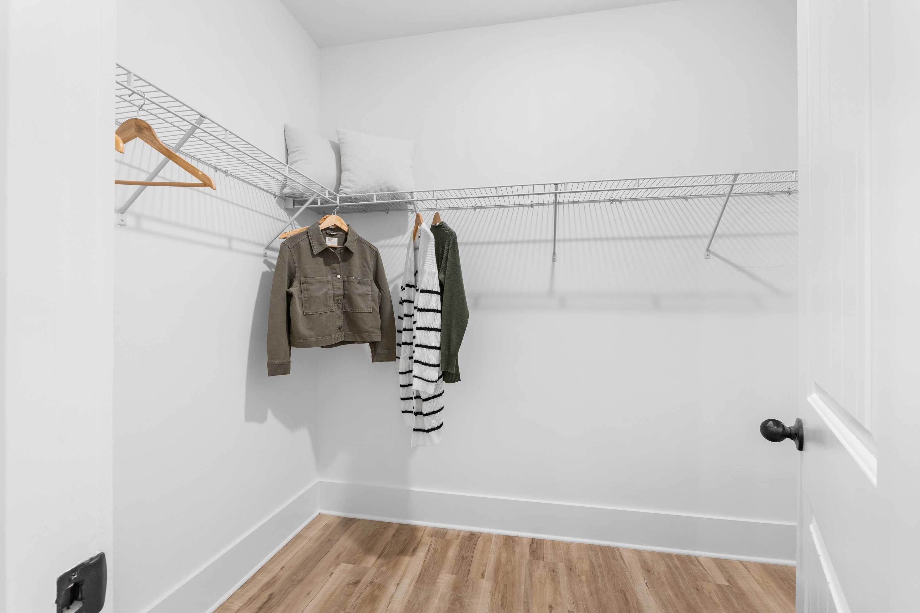 Spacious walk-in closet in Spragins Cove Huntsville AL with white walls, wire shelving, and hanging clothes on wooden hangers