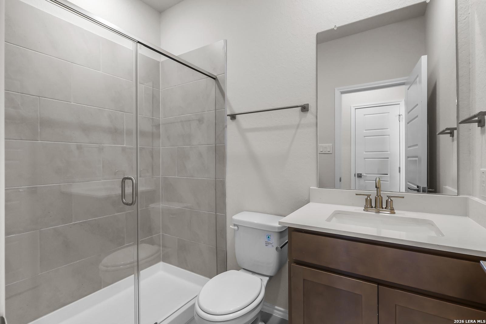 Modern bathroom with glass-enclosed shower and wood vanity in The San Marcos F floor plan at Rayburn Valley, San Antonio.