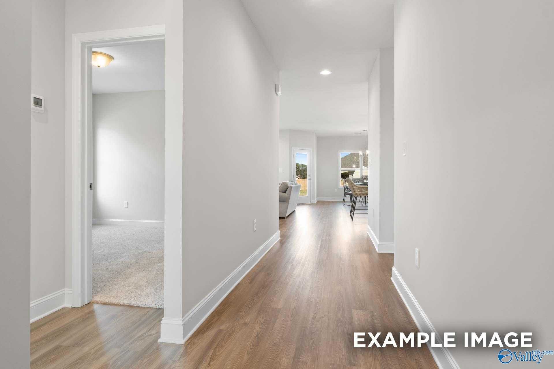 Bright hallway with hardwood floors and white walls leading to open living area in The Franklin C home, Meridianville, Alabama