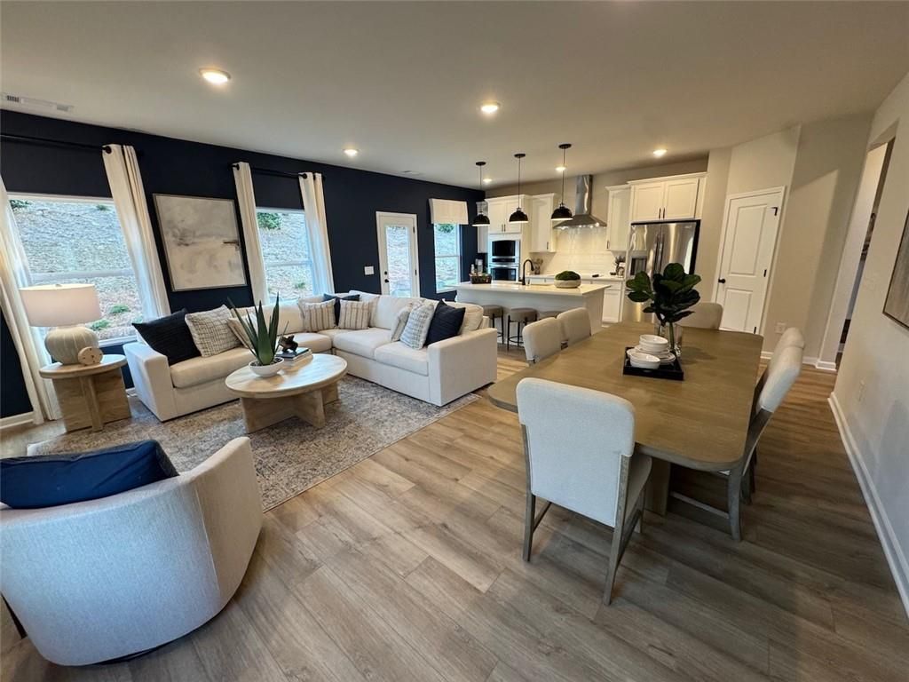 Open-concept living and dining area with L-shaped sofa, white kitchen cabinets, island bar, and hardwood floors in The Hartwell A, Canton, GA