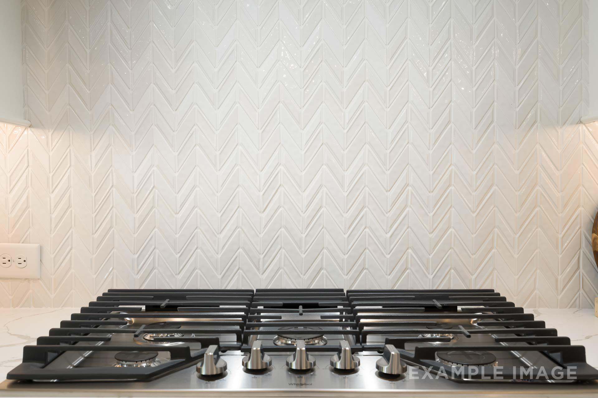Modern gas cooktop in The Seaside C gourmet kitchen with white herringbone tile backsplash and under-cabinet lighting