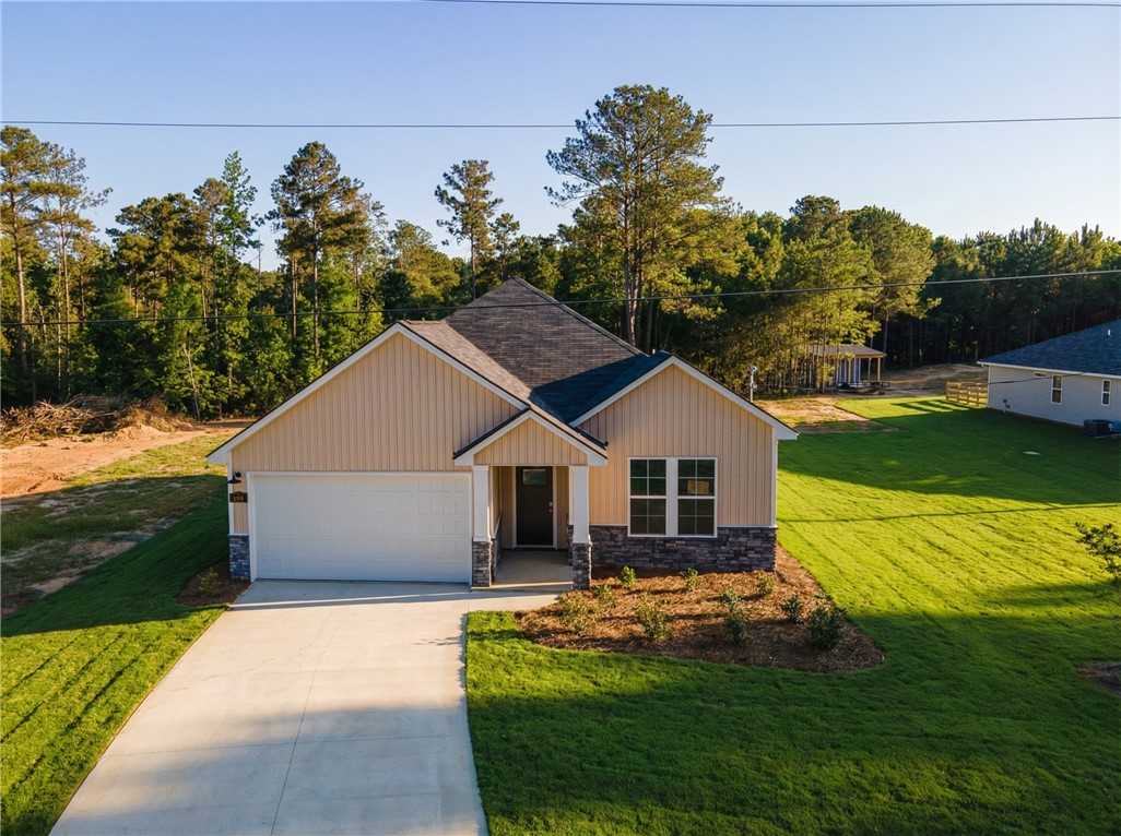 Modern beige 1-story 4-bedroom home with 1-car garage, front porch, driveway, and wooded yard in Silver Oak, Cusseta, Alabama