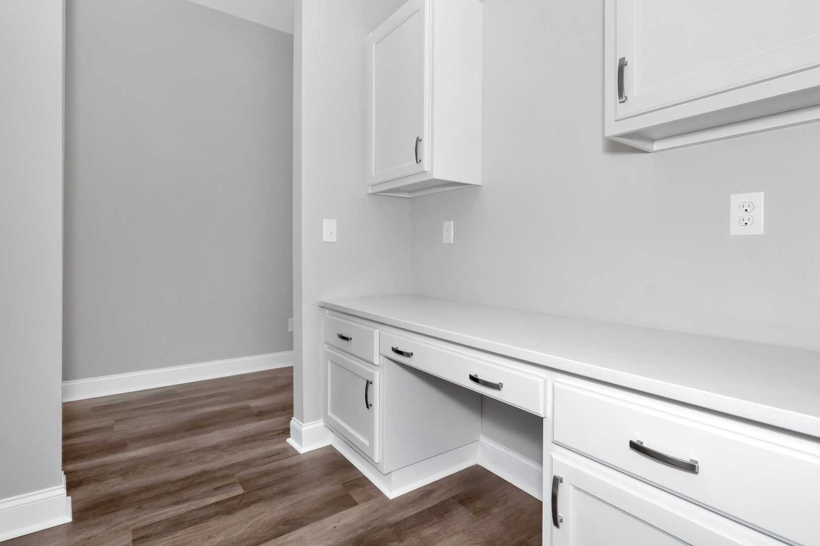 Built-in white desk and cabinetry in The Arcadia M home office, gray walls, hardwood floors, Evermore Homes