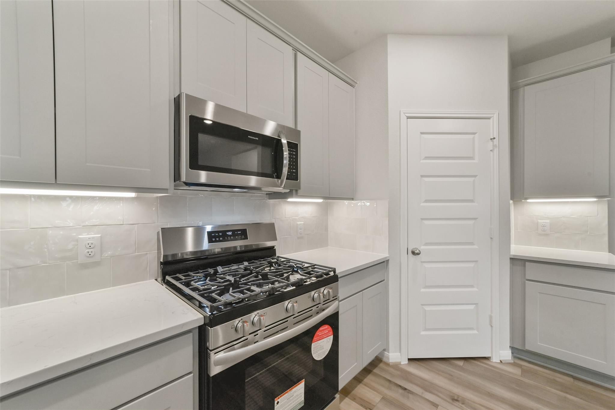 Modern kitchen with white shaker cabinets, stainless steel gas range and microwave in Davidson Homes San Marcos E, Beasley, TX